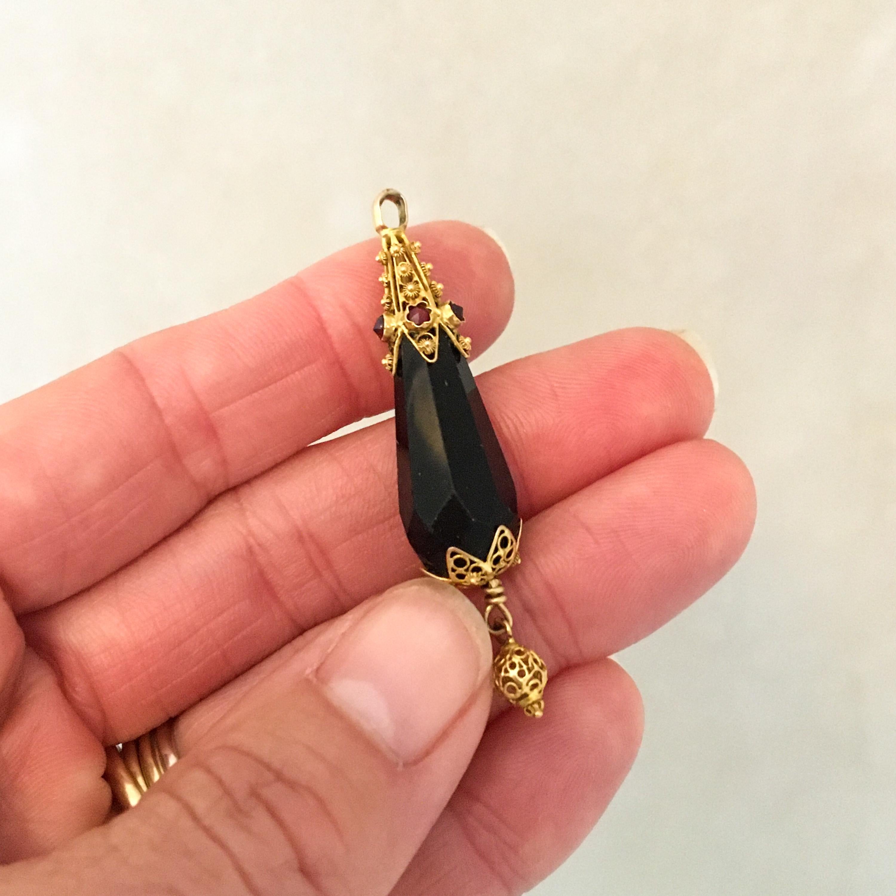 A briolette pendant made of faceted black jet and set with five garnet stones. The black jet is set between two gold filigree openwork caps. The gold cap on top of this pendant is embellished with beautiful cannetille work, filigree and five faceted