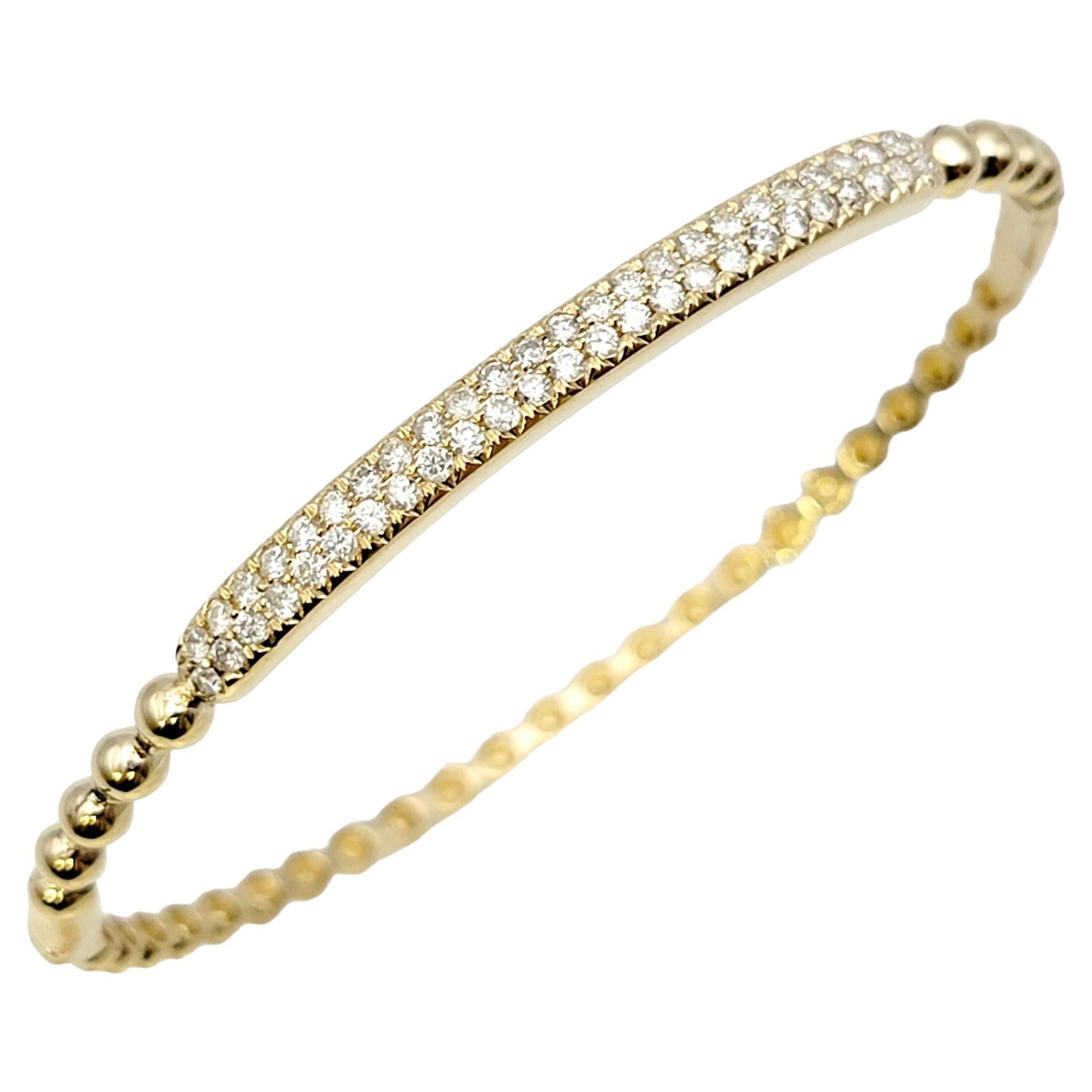 Contemporary bangle bracelet in a 14K yellow gold featuring a narrow bubble design. The top portion of the sleek bracelet is adorned with two elegant row of sparkling pave diamonds. Stack it with other bracelets for a modern look, or simply wear on