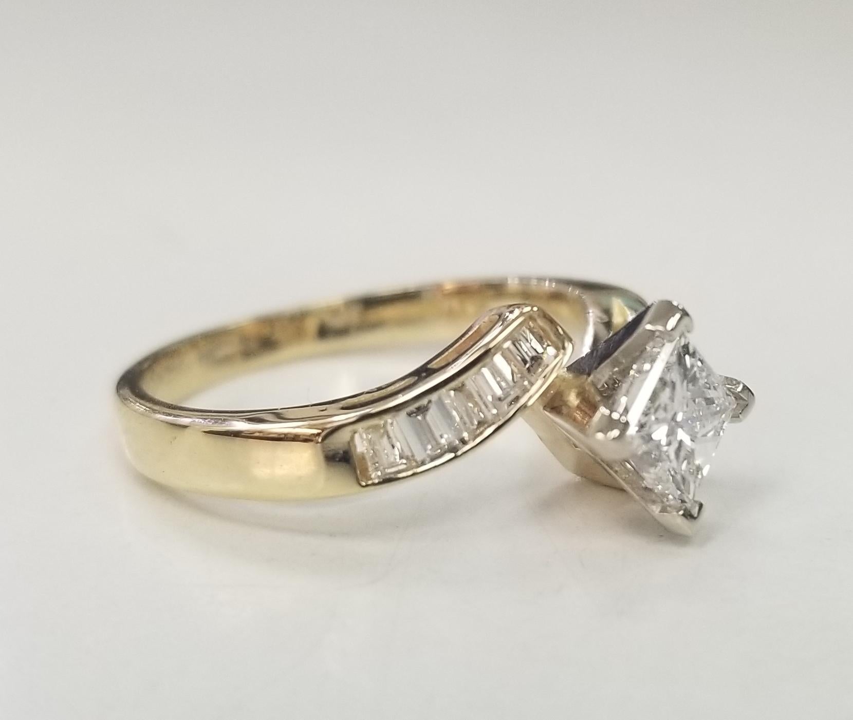 Une bague unique avec un anneau qui se chevauche pour mettre en valeur la magnifique pierre centrale ronde de 0,72 carat de couleur G et de clarté VS2. La bague torsadée à chevauchement comporte 10 diamants baguettes droits d'un poids total