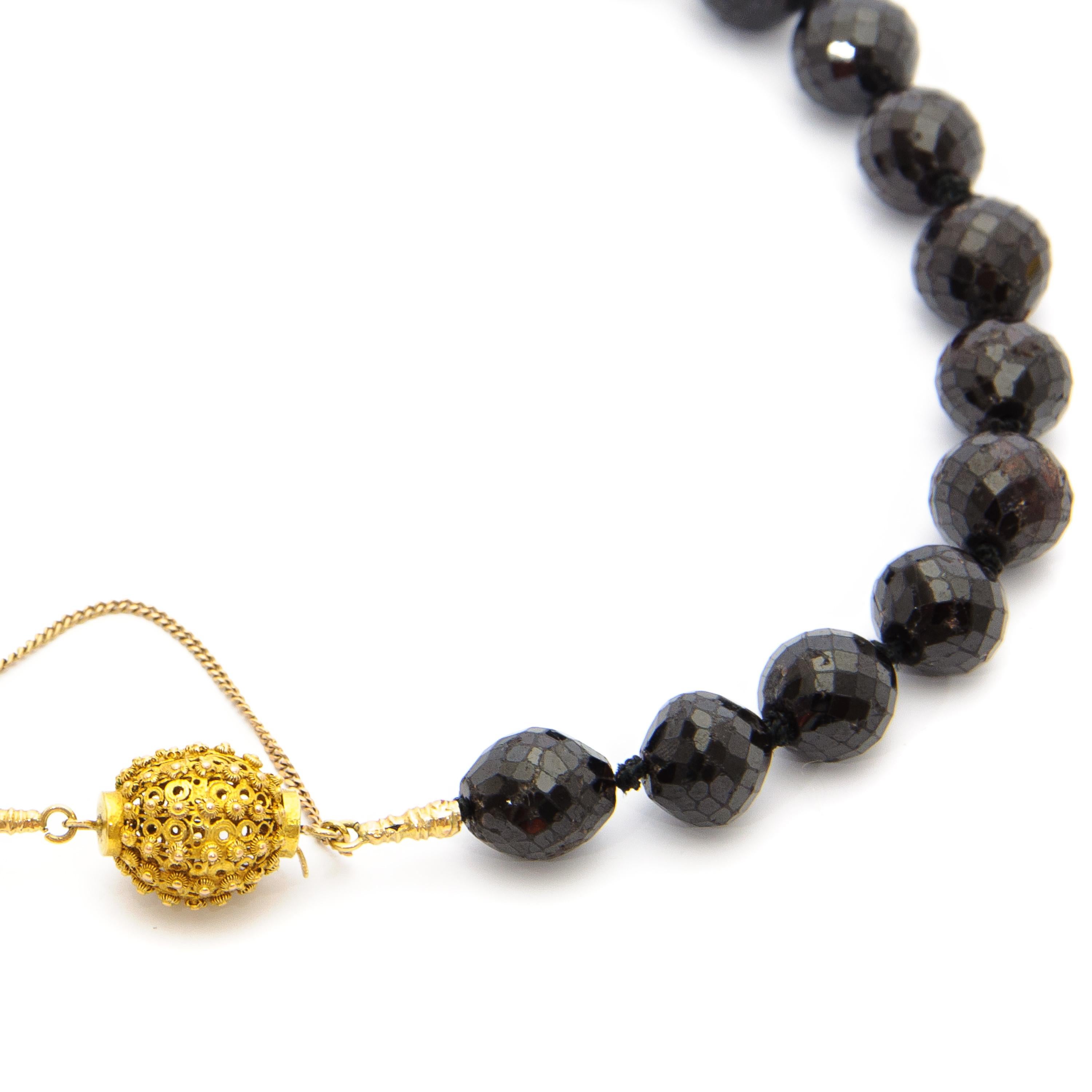 A 14 karat gold garnet necklace made of 27 round faceted garnets. The garnets have a diameter of approximately 1.4 centimeter, which are strung on a gold thread string from the lock. Between each garnet bead, the black thread is nicely knotted, to