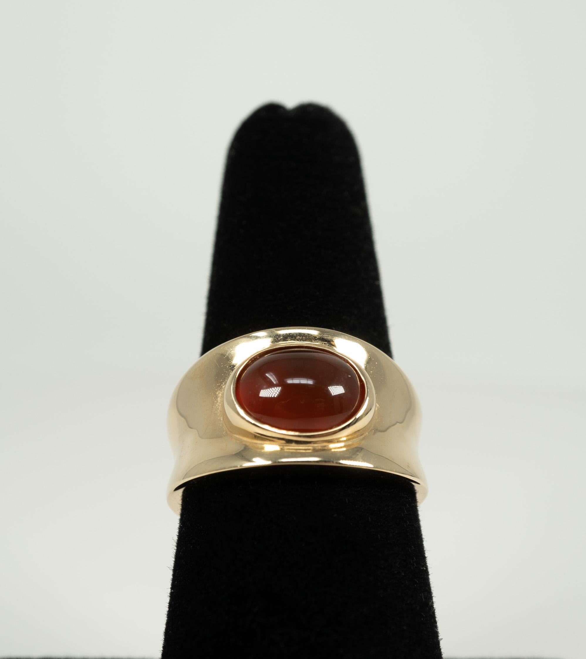 This 14 karat, highly polished, yellow gold, mounting is centered with one bezel-set, oval-shaped, cabochon-cut carnelian stone. 