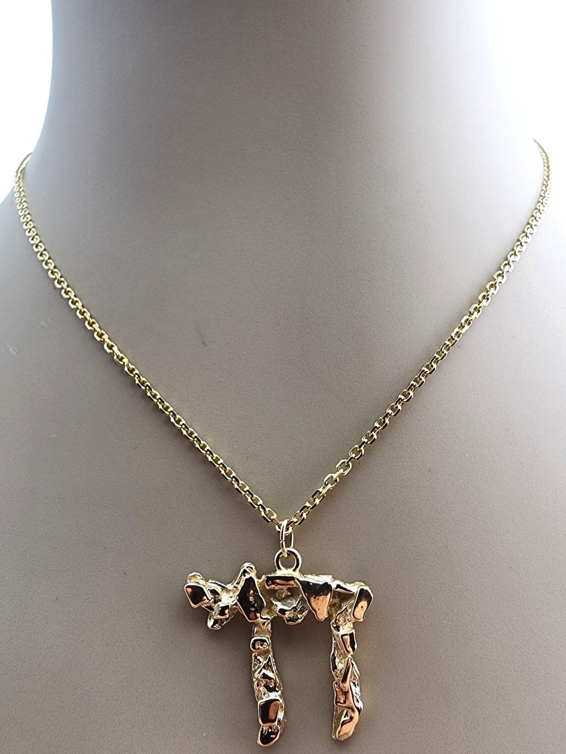 14 Karat Yellow Gold Chai Nugget Pendant-

This 14 karat yellow gold Chai nugget pendant features a bold, textured nugget design paired with the meaningful Hebrew symbol for “life.” Its polished finish and unique shape give it a strong, eye-catching