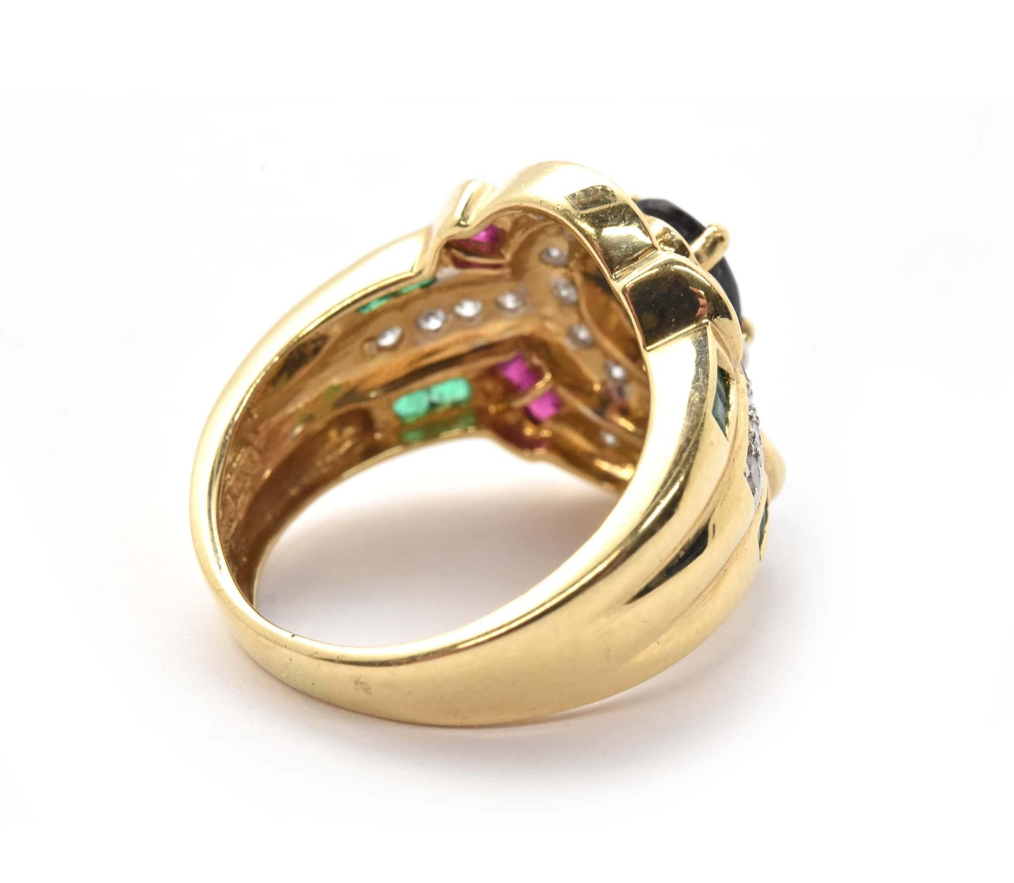 This ring is made in 14k yellow gold, and it holds an oval sapphire at its center. The stone measures 7×5.2mm. The sapphire is surrounded by small round diamonds along with ruby and emerald accents for a splash of color. The diamonds have a total