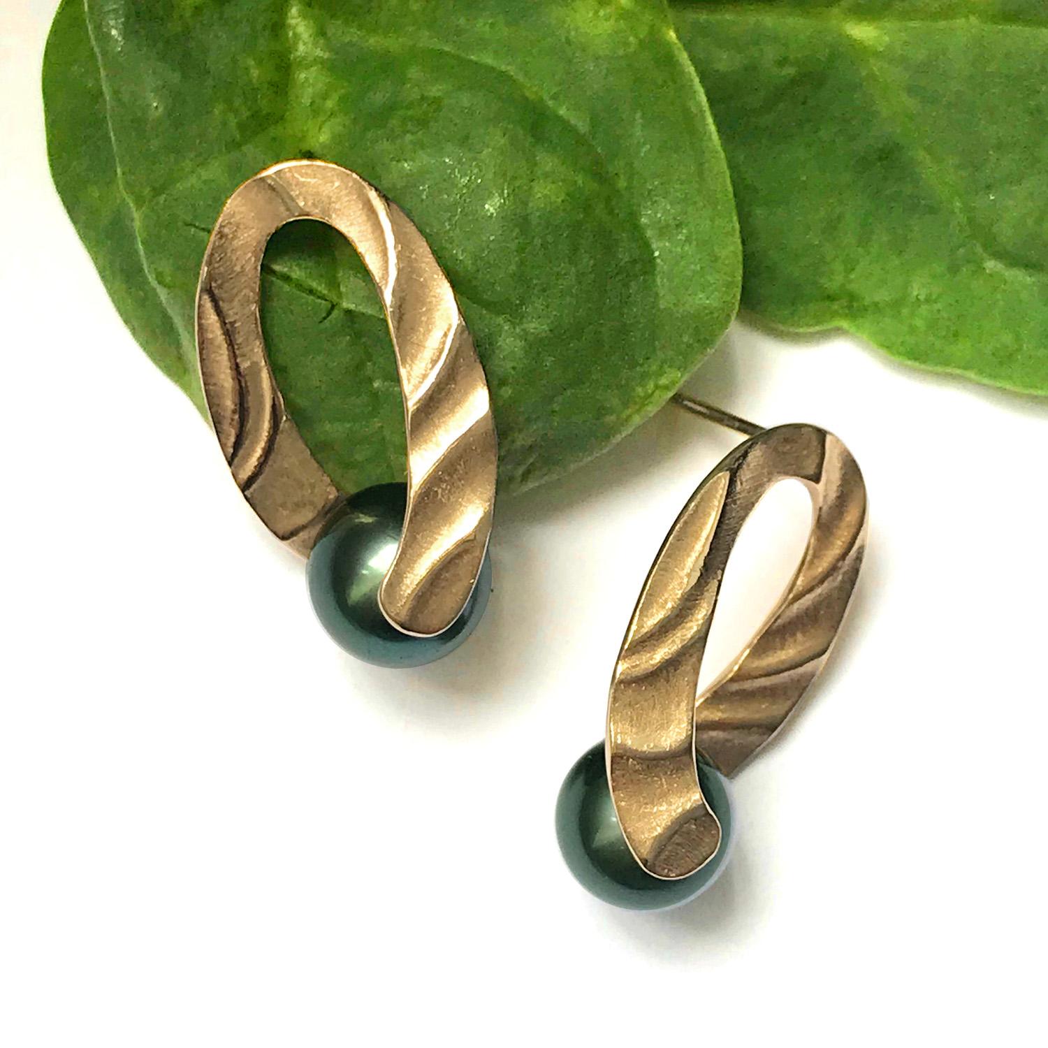 K.Mita's Holding You Earrings, which are 26 x 13 x 14mm and made from 14k Yellow Gold, twist slightly as they grasp a 9-10mm Tahitian Pearl. The Sand Dune texture, with its undulating patterns, highlights the efforts we make to hold on to what is