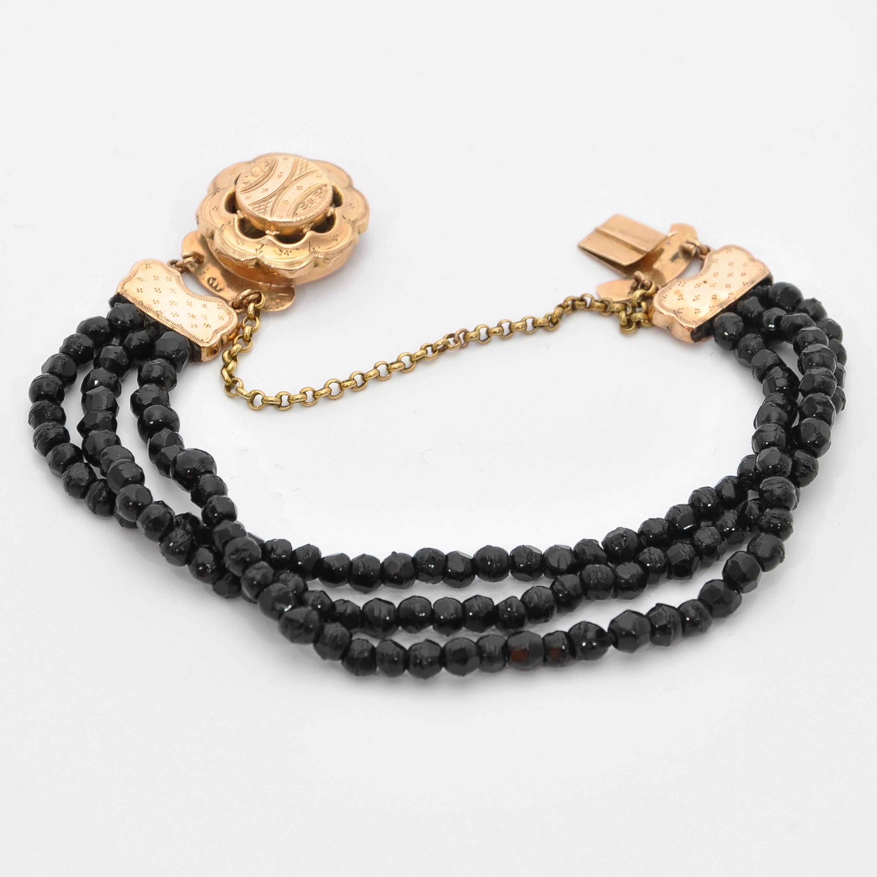 14 karat yellow gold black jet bracelet with a beautifully etched round clasp. The bracelet is made of three-strands, the beads are made of faceted jet. The clasp has an etched design on top with an openwork design in the center which represents a