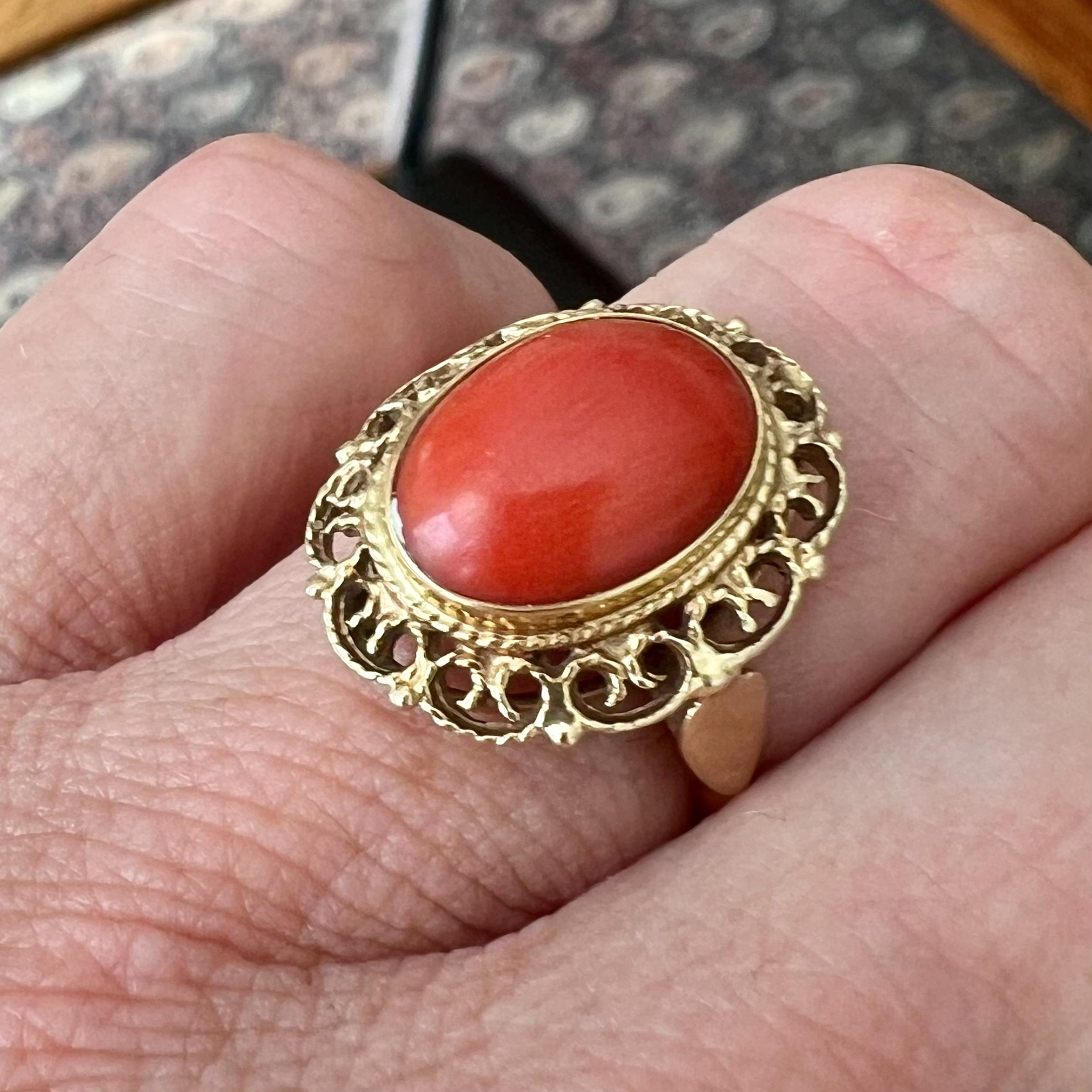 A vintage 14 karat yellow gold natural coral ring. The oval-shaped frame of the ring is beautiful and has a detailed openwork filigree design. The stone is bezel set in a 14 karat gold frame, lovely detailed with a rope motif around the rim of the