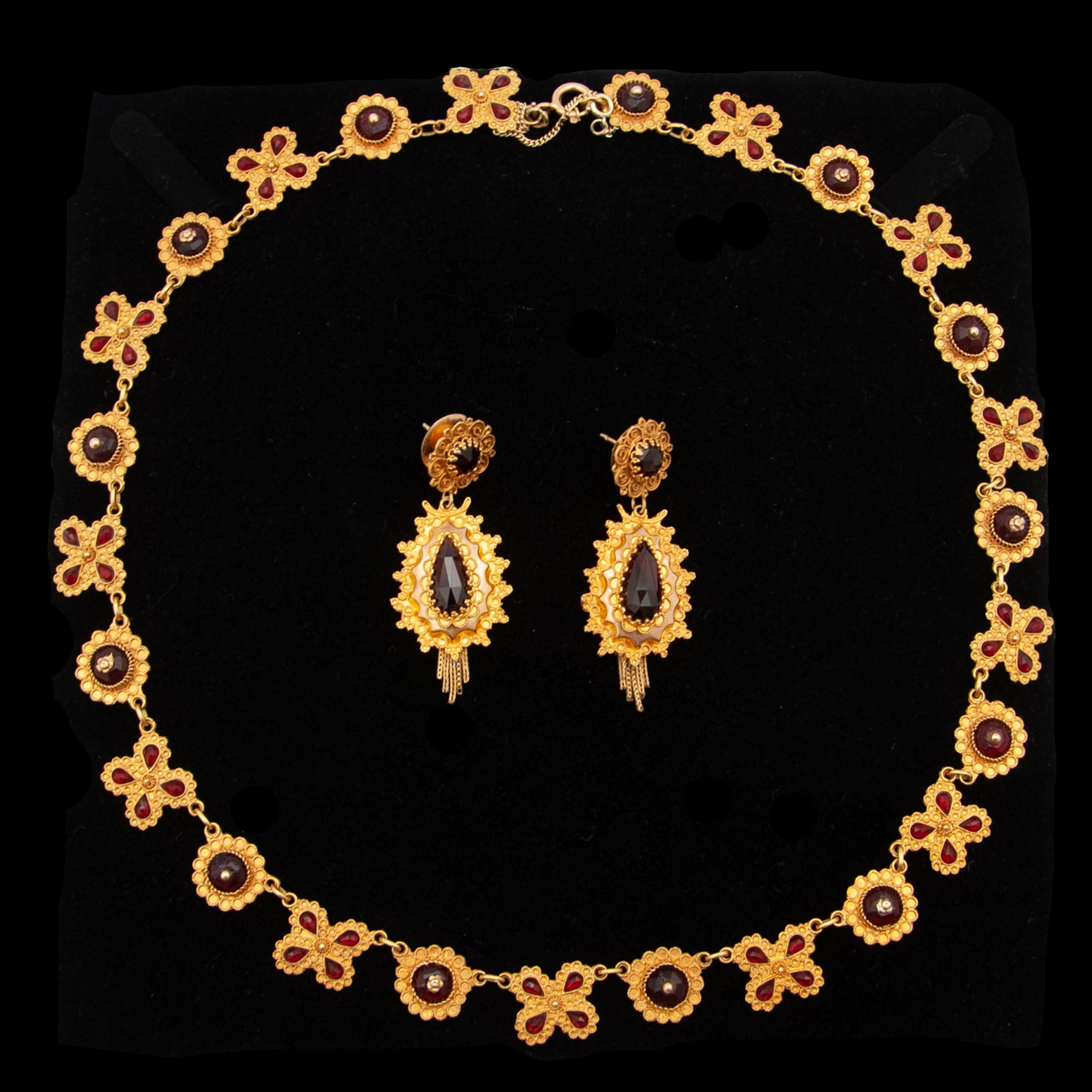Magnifique parure ancienne en or du 19e siècle composée de boucles d'oreilles et d'un collier. Le design du collier est époustouflant. La chaîne du collier alterne avec une fleur d'or et une rosette. Les fleurs sont incrustées de quatre grenats en