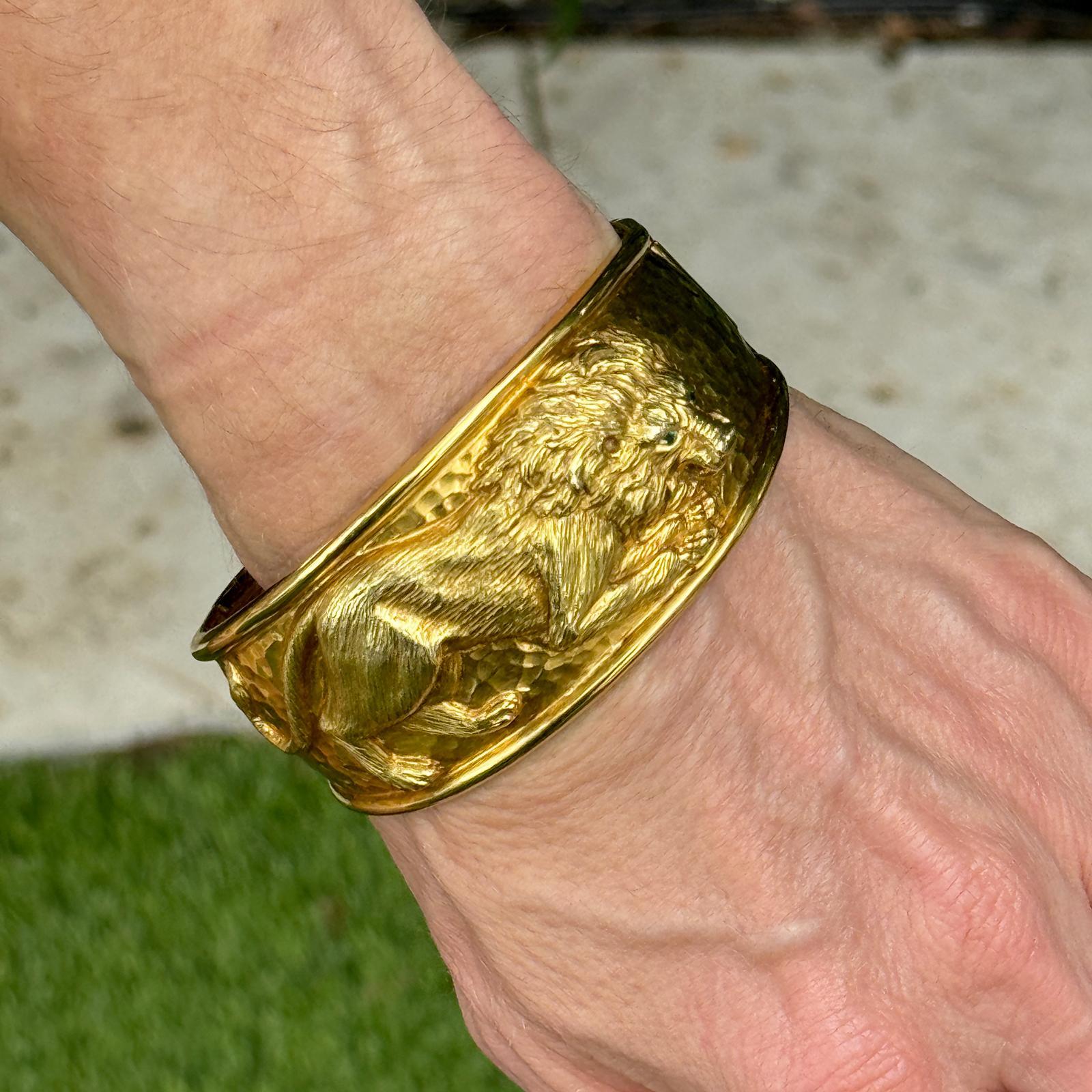 The Yellow Gold Bangle bracelet features a striking lion motif with captivating emerald eyes. This exquisite piece combines the rich warmth of 14 karat yellow gold with the regal design of the lion, adding a touch of bold elegance. The detailed
