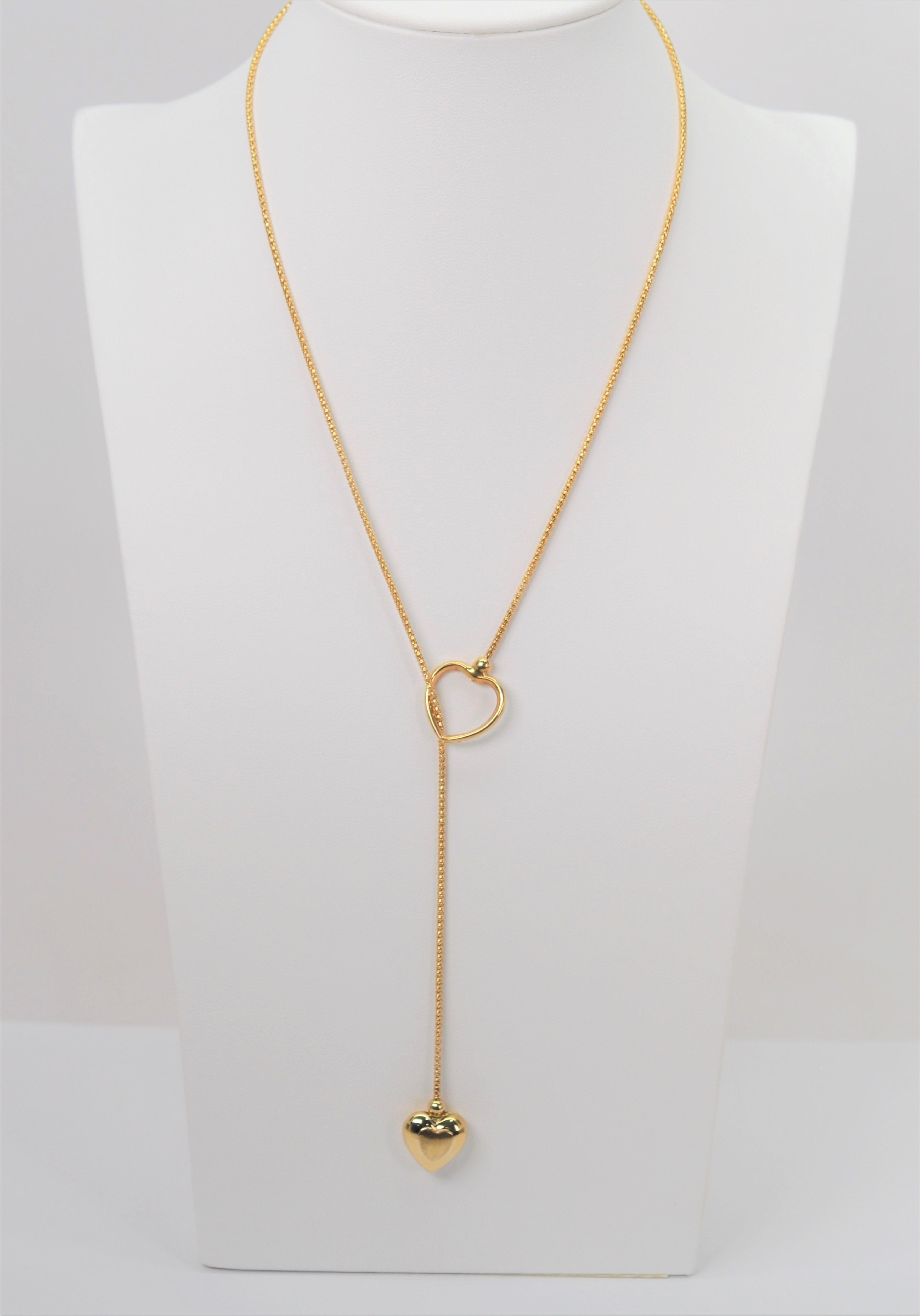 A soft twenty inch round mesh chain of fourteen karat 14K yellow gold hosts companion gold heart charms that thread to create the adorable dangling heart drop of this Italian made lariat style necklace. Adjustable and stylish with wide appeal for