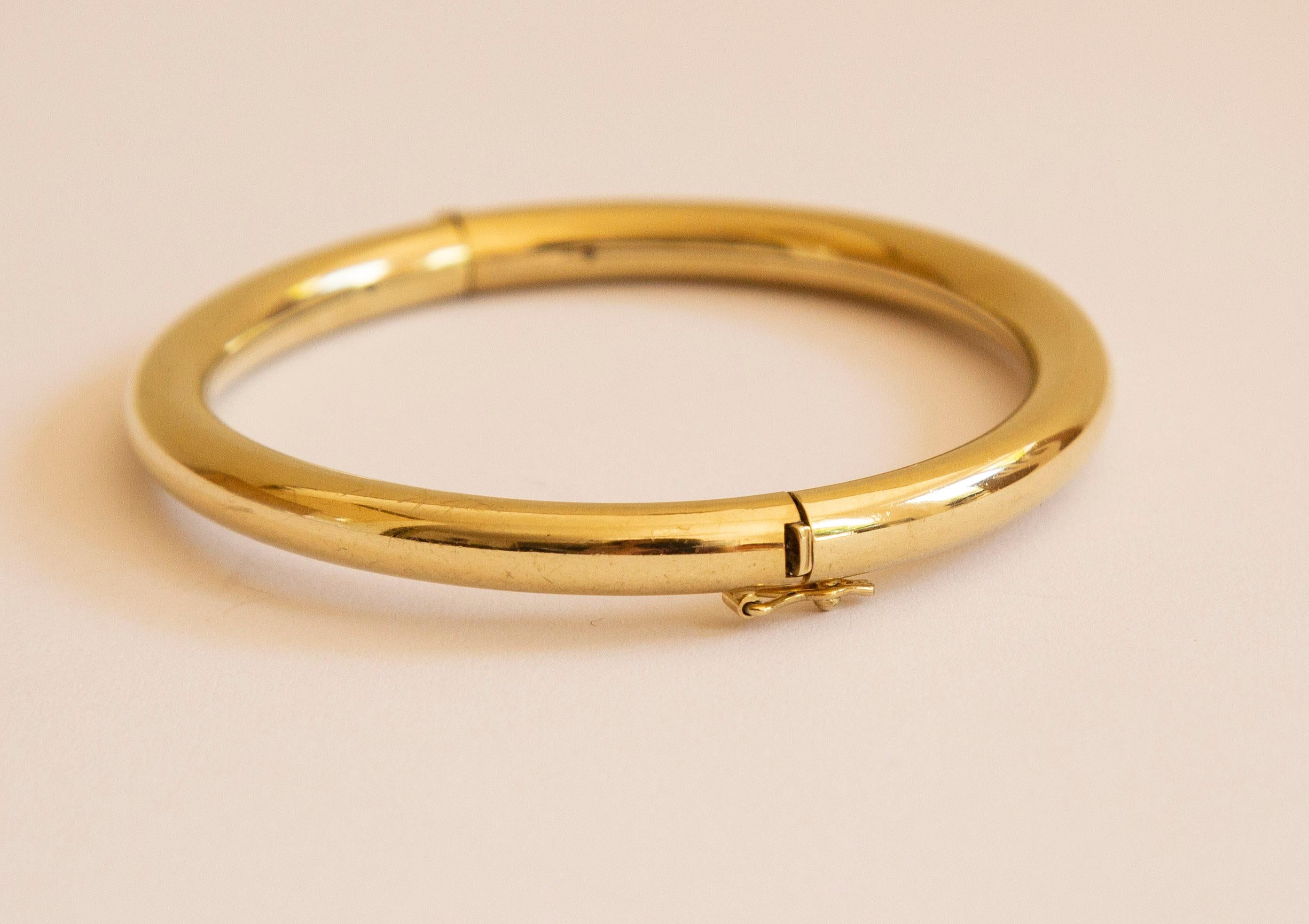 A vintage bangle, rigid bracelet made of 14 karat solid yellow gold. The bracelet features a hinge in the middle and a box clasp and safety figure eight lock. The bracelet is in good vintage condition with superficial tiny and fine scratches visible