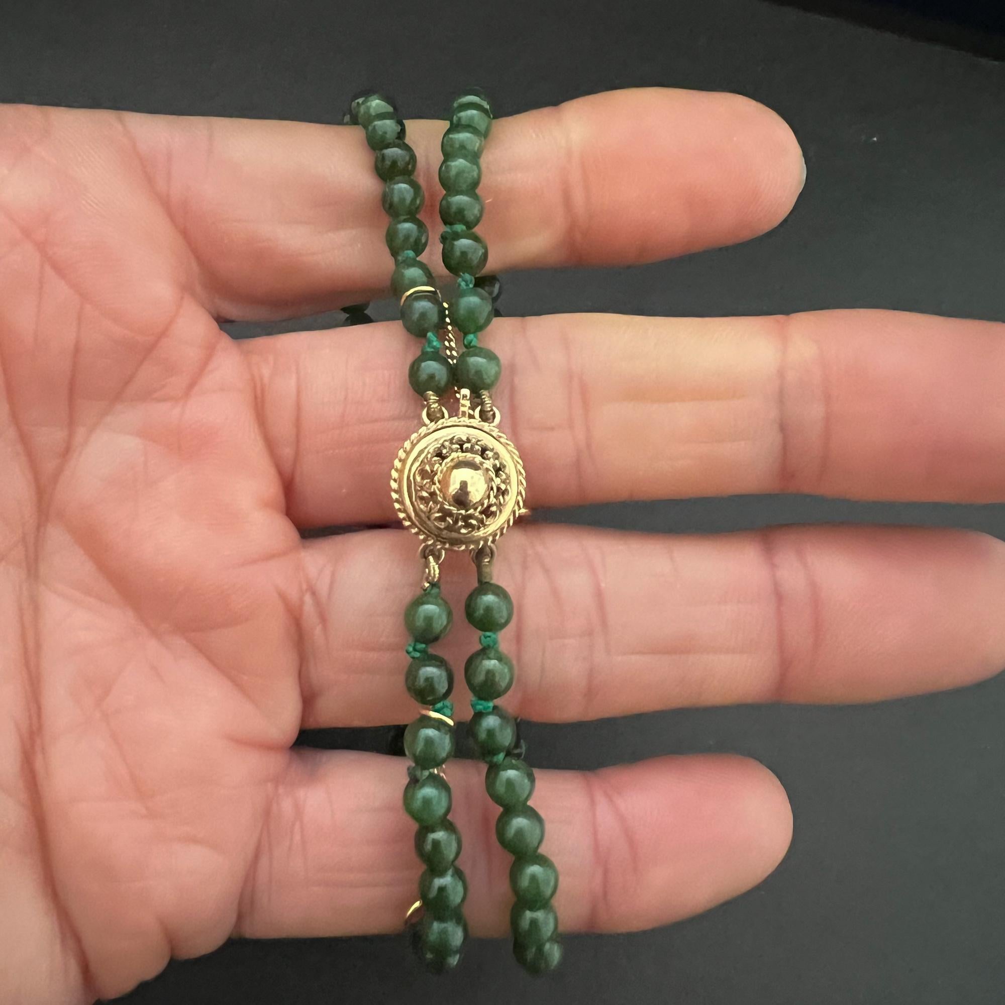 A natural jade 14 karat gold two-strand beaded bracelet. The jade beads of this bracelet are round-shaped and are beautifully mottled with different hues of dark green. The round gold clasp has a fine openwork structure with a gold dome in the