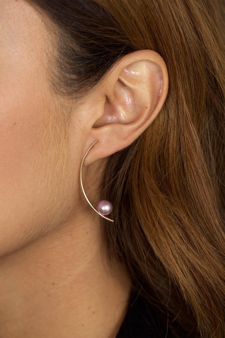A luminescent pink pearl sits balanced on the edge of curved 14k yellow gold in these dangling stud earrings.  Bold yet delicate, these earrings are a perfect compliment to a streamlined modern look and a stylish example of the versatility of