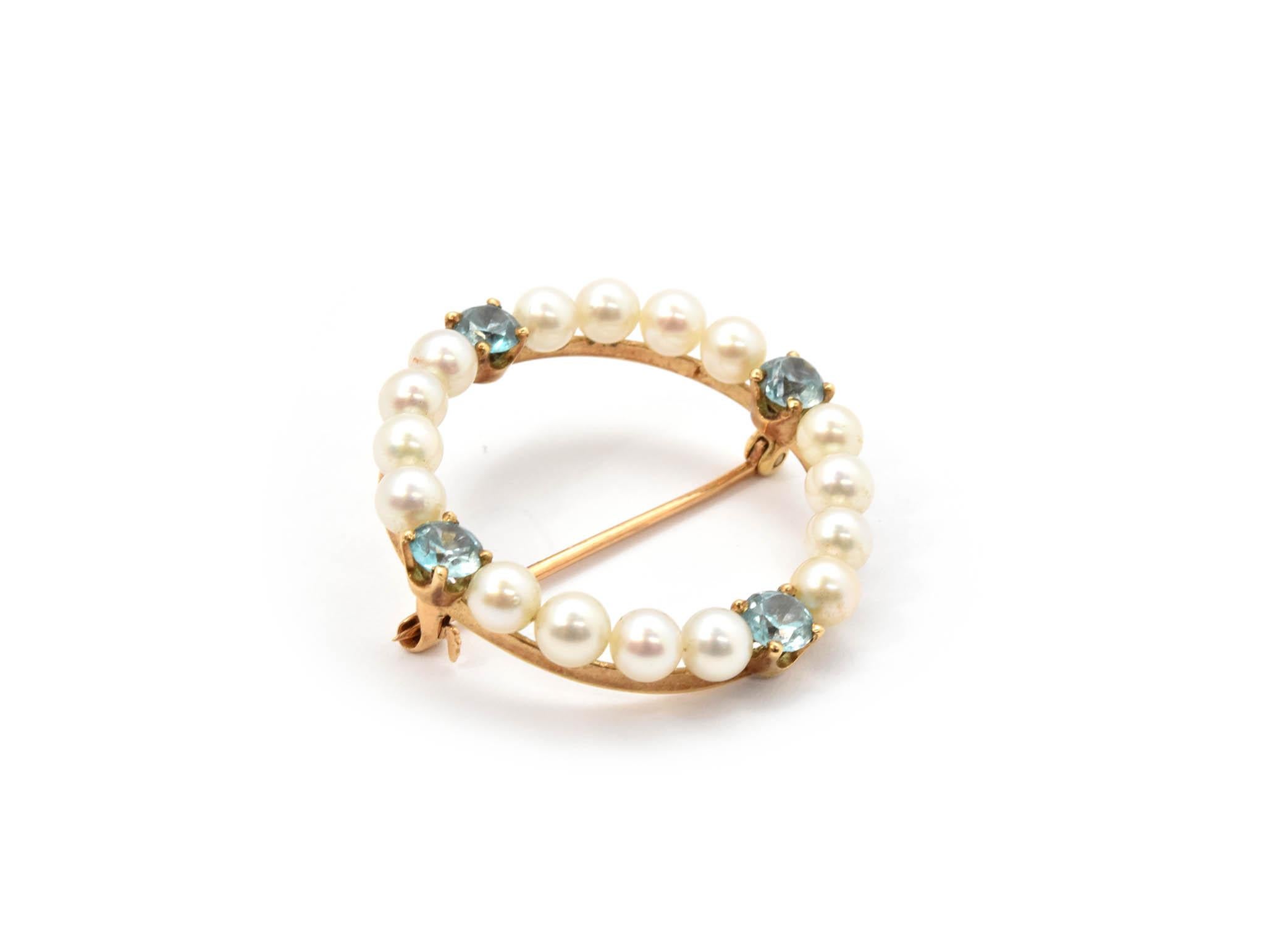 This brooch is made in 14k yellow gold, and it features white pearls accented by 4 blue zircon gemstones. The brooch measures 29mm in diameter, and it weighs 4.0 grams.