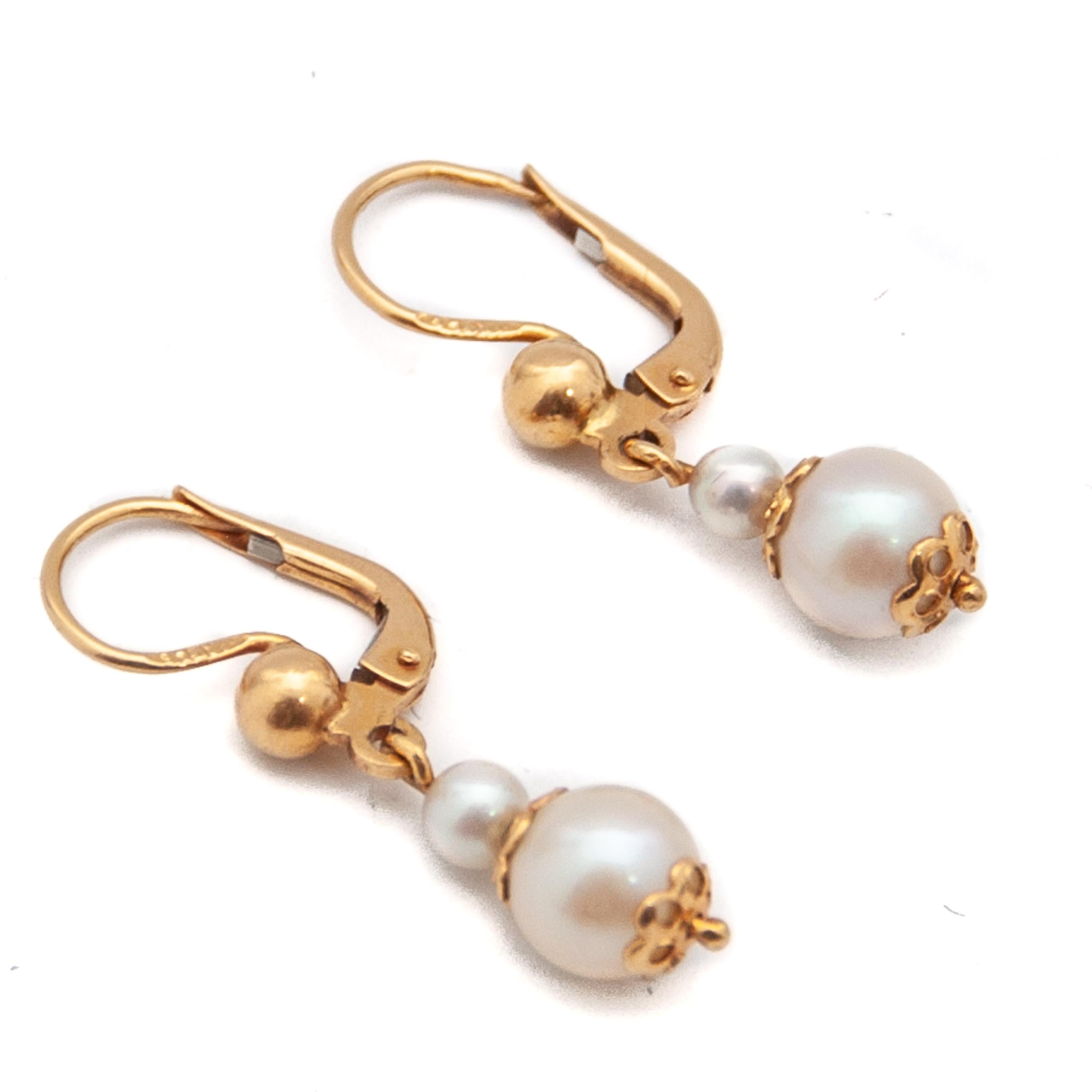 Pair of pearl drop earrings crafted in 14 karat gold. These lovely vintage drops are made with two round pearls set with a gold openwork flower design at the centerpiece and bottom. The earrings have a lever-back closure with a golden sphere.

The