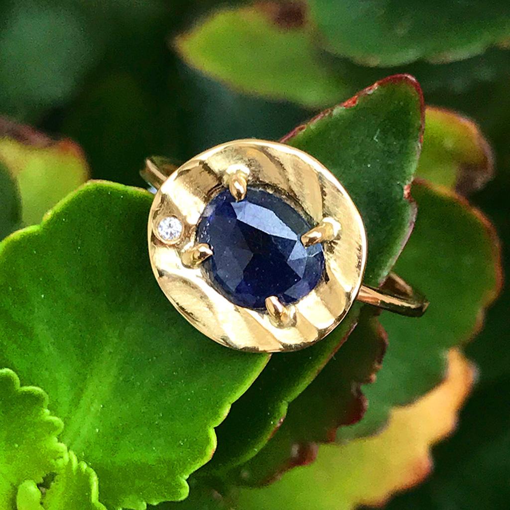 La petite bague galet en or jaune 14 carats, unique en son genre, de K.Mita est ornée d'un saphir bleu à taille rose de 0,725 carat, rehaussé d'un diamant de 0,01 carat. La bague contemporaine, fabriquée à la main par l'artiste, mesure 12 mm à son