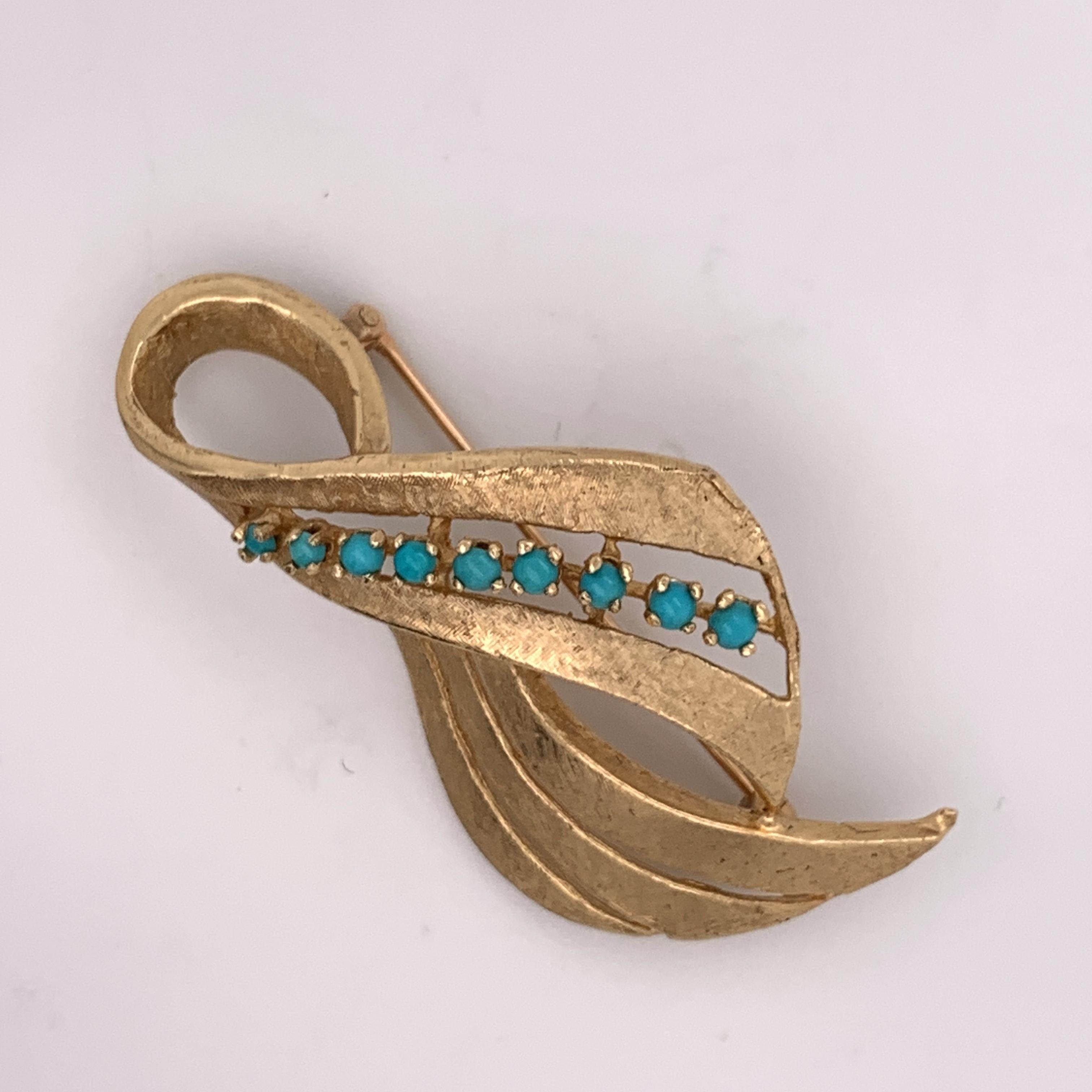 This gorgeous statement brooch can also be worn as a pendant. The main shape of the brooch is that of a criss-cross ribbon of glittering textured 14K yellow gold. It features nine lovely little turquoise buttons set along the center of the top swoop