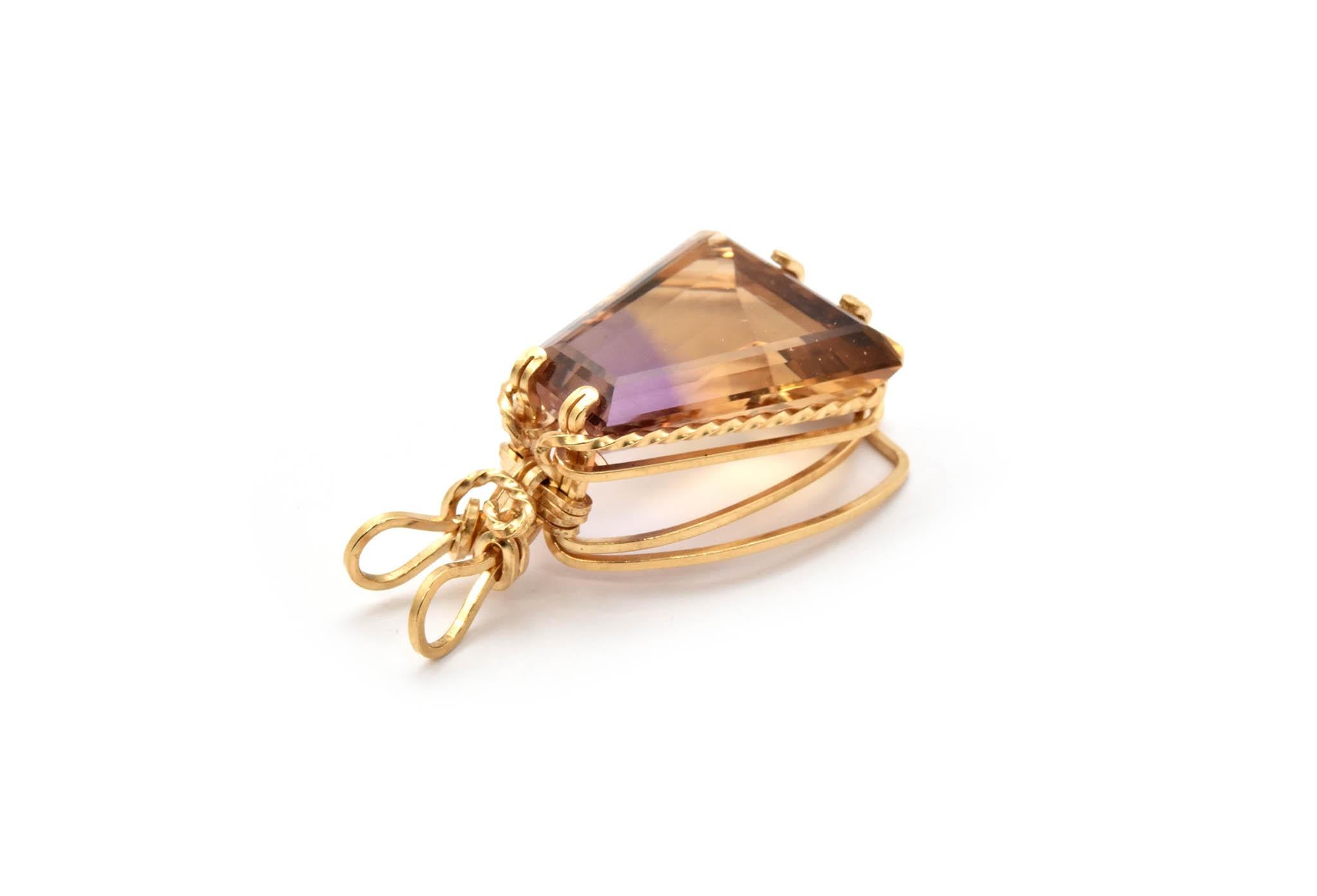 This 14k yellow gold wire wrapped pendant holds a four-sided polygonal faceted ametrine. The ametrine measures 19x8.9x21.2mm. The pendant is 39.2x22.2mm and weighs 5.7 grams.