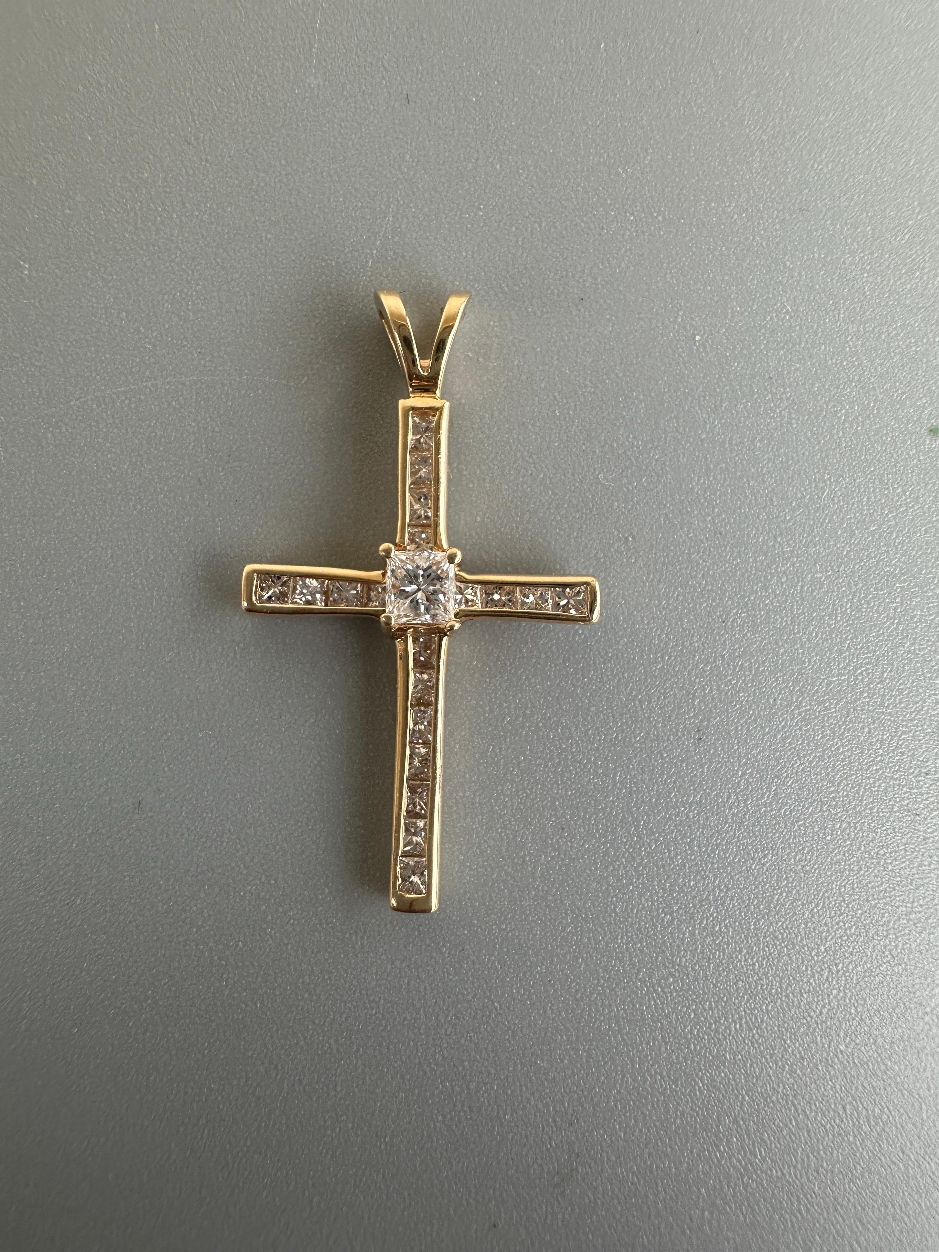 Questo ciondolo a forma di croce in oro giallo 14K è caratterizzato da un diamante taglio principessa da 0,95 carati incastonato a canale con una purezza VS e un colore G. Con un diamante centrale più grande e un design classico, questo ciondolo è