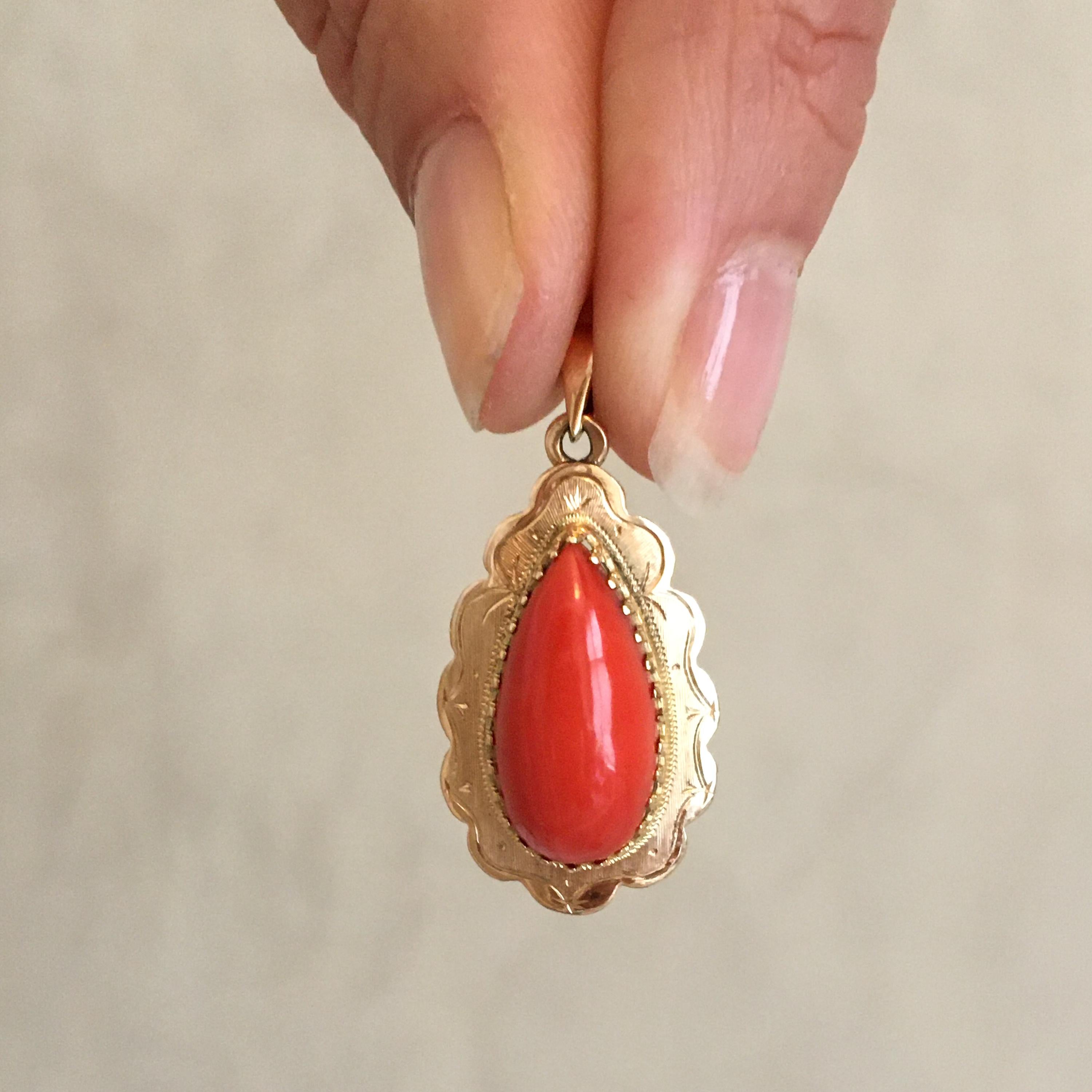 A 14 karat yellow gold pendant set with a large natural coral drop-shaped cabochon. The border of the pendant has a beautiful scalloped design and etched fantasy motifs at its surface. The coral cabochon is bezel set.  

The *coral pendant is in