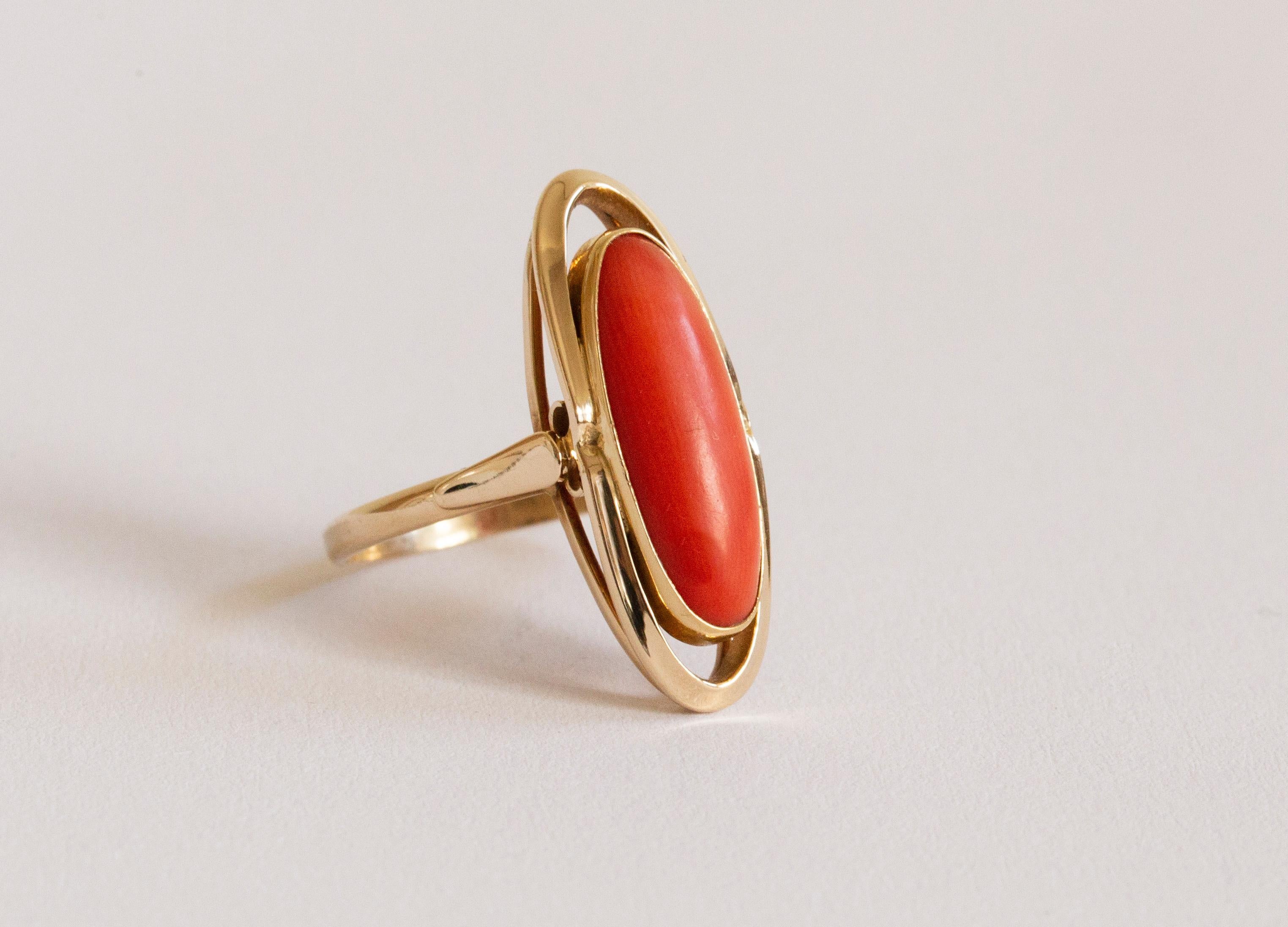 A vintage (ca. 1980s) 14 karat yellow gold with natural red coral cabochon. The ring features an elongated shape and the red coral is set in a smooth frame with a halo. The ring is marked 585 that stands for the 14 karat gold content.