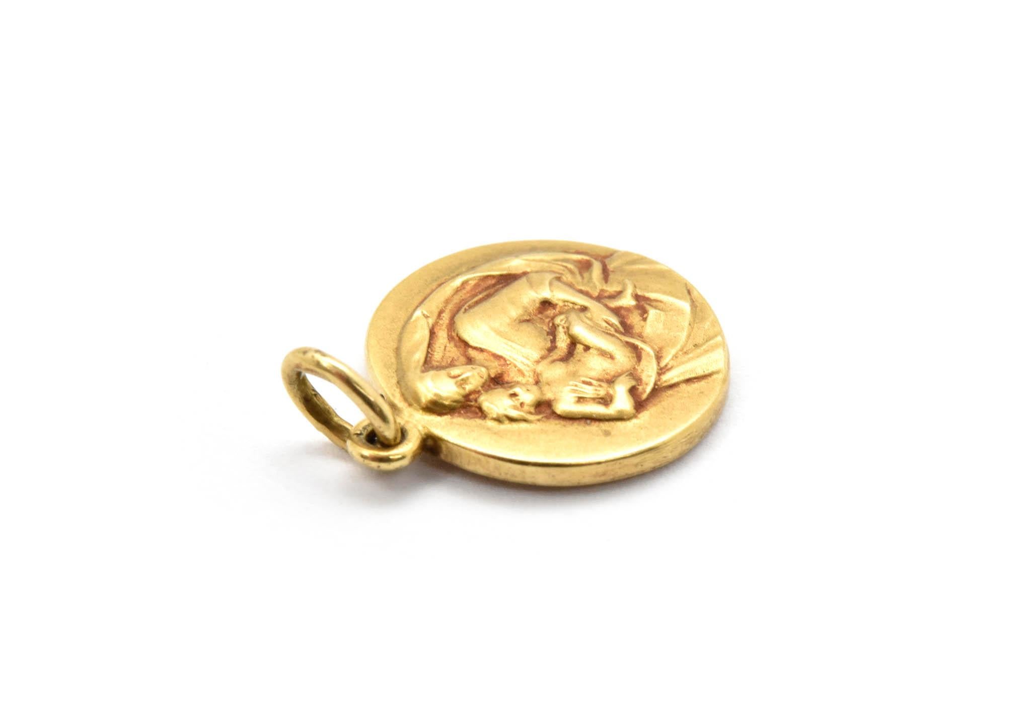 This charm is made in 14k yellow gold, and it depicts the Virgin Mary with a child in her arms. The back of the charm is engraved 