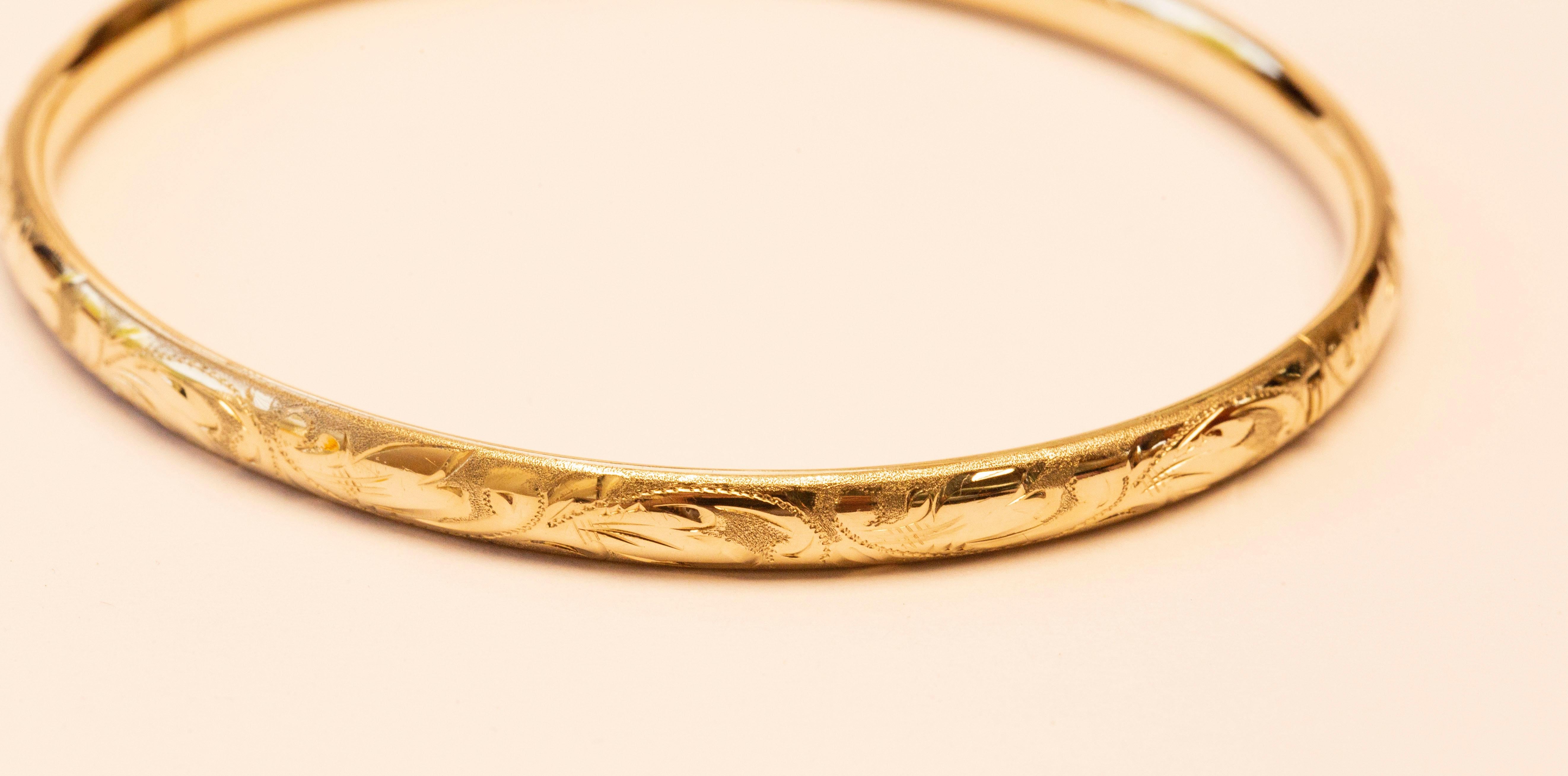 A vintage 14 karat solid yellow gold bangle bracelet with engraved floral and leaf decoration. The bracelet was made in the 1960 and it features a retro vibe that can be matched with classy as well as modern outfits.  The bracelet is in very good