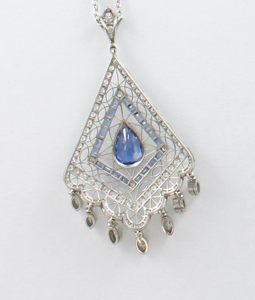 A bezel-set 4.05 ct pear-shaped natural blue sapphire is the focal point of this magnificent 14 kt white gold openwork lavaliere. It is trimmed by a diamond-shaped design of 20 bezel-set natural blue sapphire baguettes with a diamond at each corner.