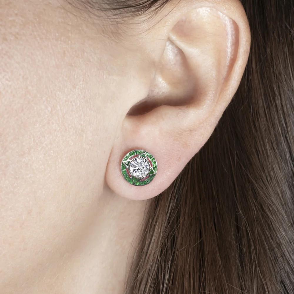 Questi squisiti orecchini con diamanti e smeraldi presentano una coppia di diamanti naturali da 1,40 carati in un iconico design Art Deco. I diamanti tondi brillanti sono luminosi e bianchi, di colore E-F, con inclusioni accuratamente posizionate