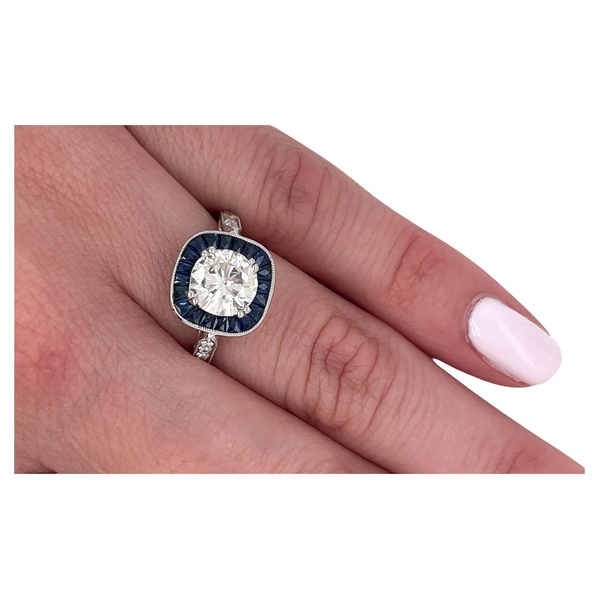 Atemberaubender Ring im Vintage-Art-Deco-Stil, der mit einem 1,40-karätigen, natürlichen, rund geschliffenen Diamanten in der Mitte besetzt ist. Dieses Schmuckstück ist mit einem Halo aus blauen Saphiren im Baguetteschliff geschmückt, der einen