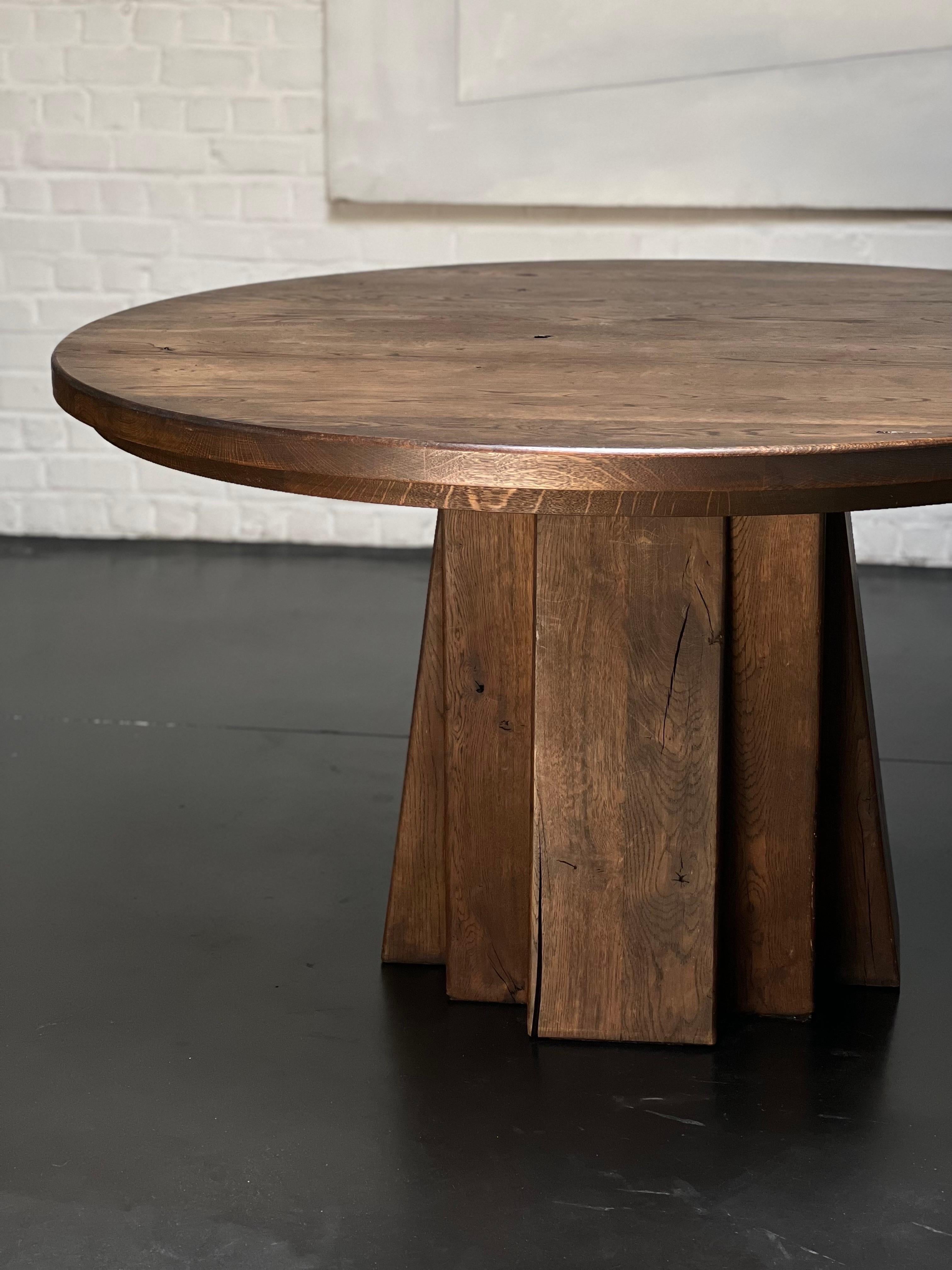 Very unique stained massive handmade oak dining table. The top is 140 cm in diameter and the height is 77 cm.  The top is lightly patinated and shows various shades of brown/brownish colors Elegant and brutalist describe that table properly. Very