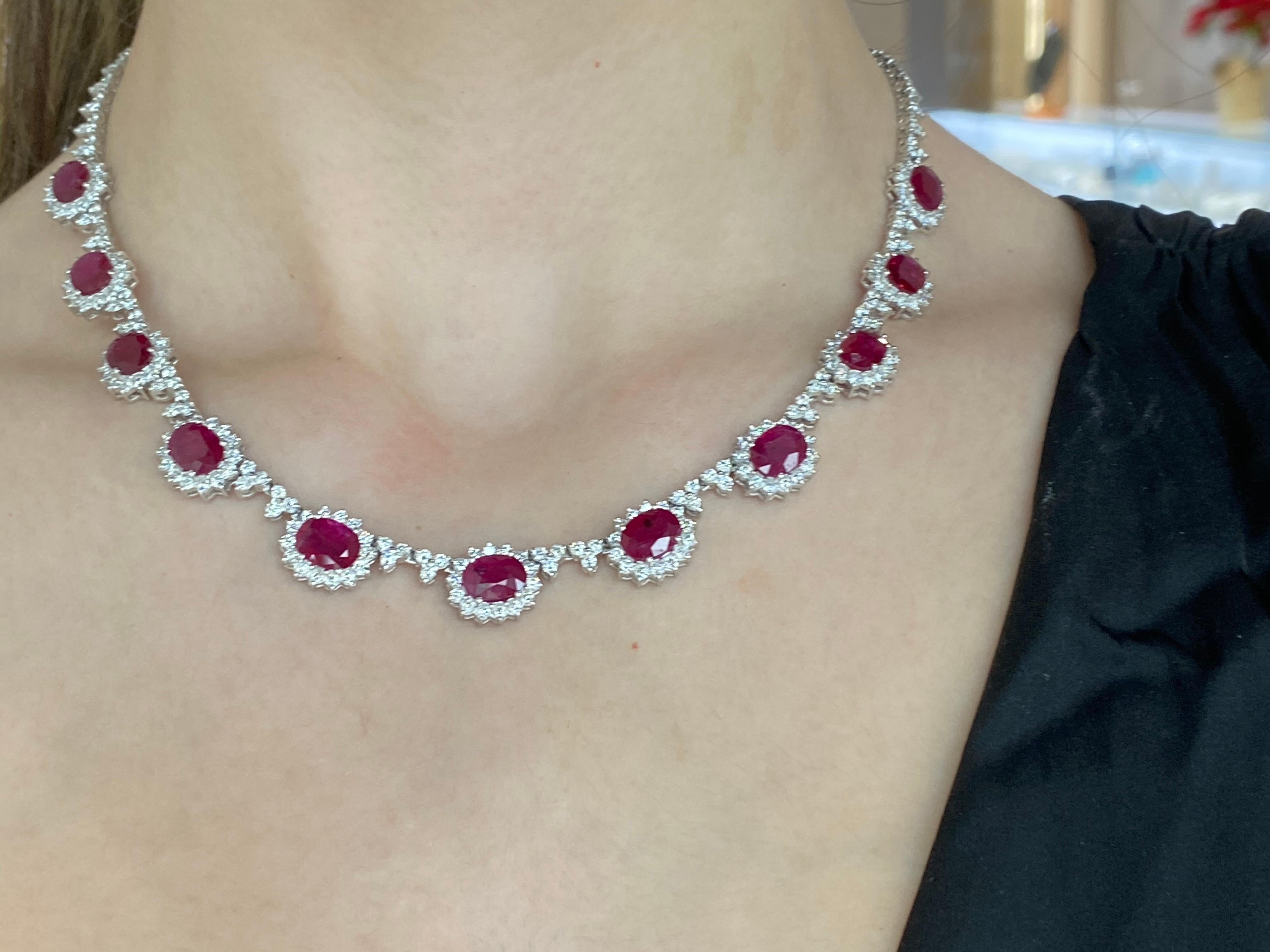 This exquisite necklace is adorned with 14.07ct total weight in 11 oval shaped vivid red natural rubies surrounded by 8.03ct total weight in round diamonds forming halos around each ruby and along the chain. The necklace is approximately 16 inches