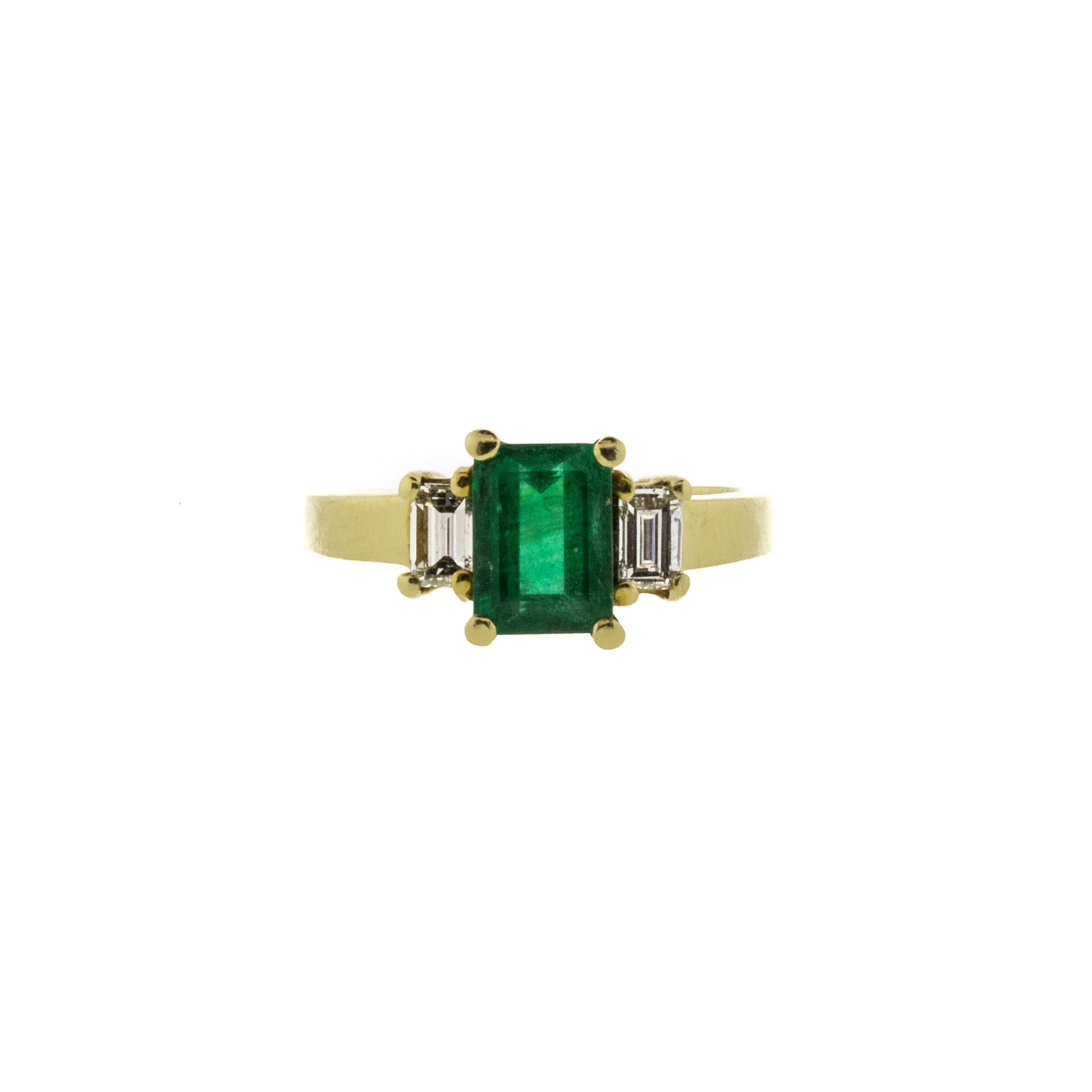 A deep forest green 1.40 carat Zambian emerald takes center stage in this unique vintage ring. Flanked by two .25ct G-H/VS straight baguette natural diamonds, the traditional emerald-cut center and oversized prongs give this ring a geometric