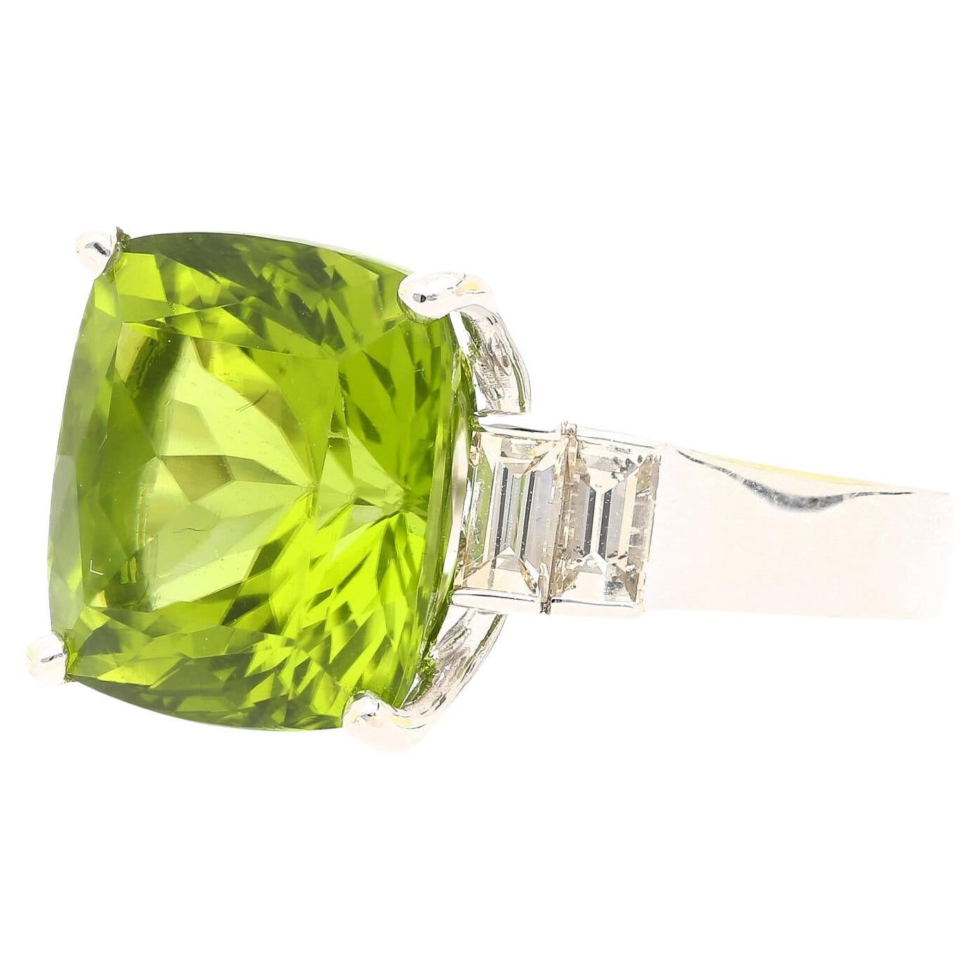 14.11 Carat Cushion Cut Green Peridot and Baguette Cut Diamond Side Stone Ring in 18K White Gold. This sophisticated ring features a peridot center stone with two baguette-cut diamonds on each side. The peridot boasts exceptional brilliance and is