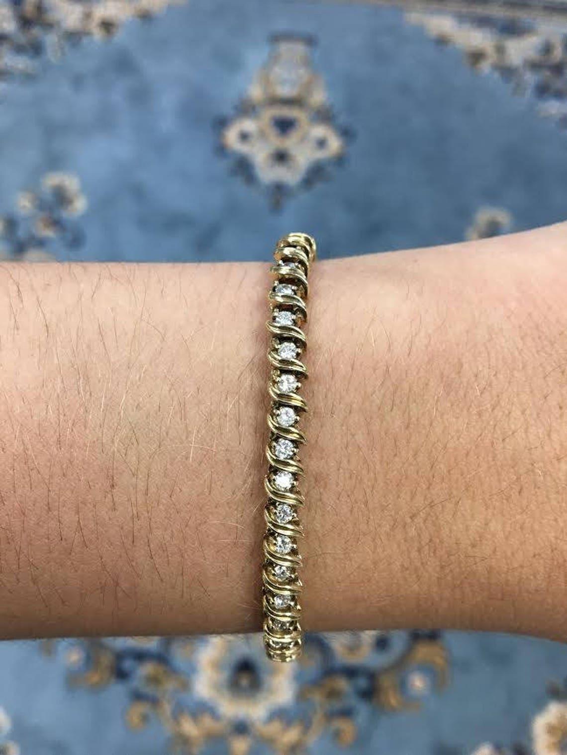 Gorgeous diamonds immediately catch your attention upon seeing this bracelet. A classically styled diamond solid gold tennis bracelet. Displayed are alternating diamonds accented by S shaped golden accents. Each gemstone shares similar