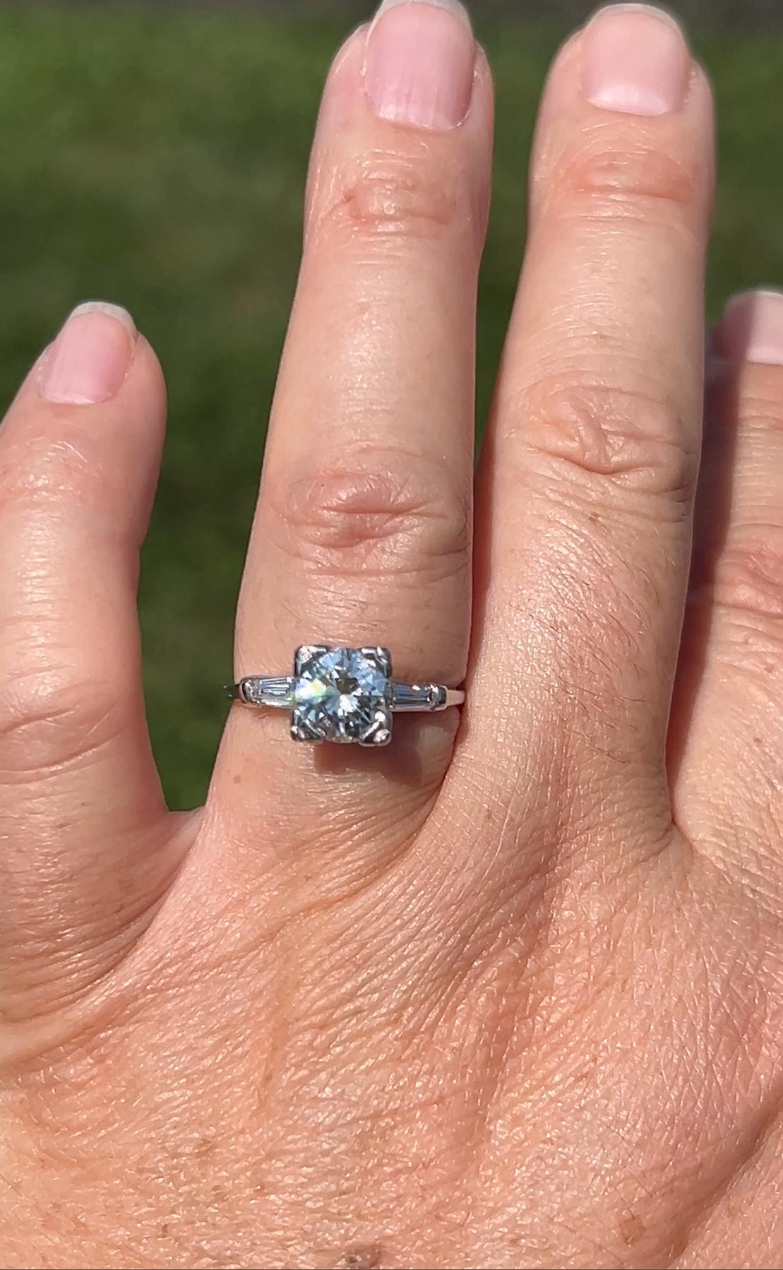 This elegant 1950s platinum engagement ring features a stunning transitional cut round diamond, approximately 1.42 carats with I color and SI1 clarity, set in an eye-catching illusion setting that enhances its size and brilliance.  Flanked by two