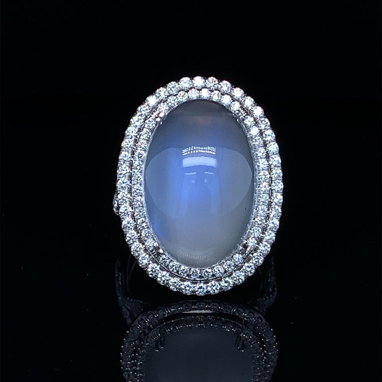 This alluring 18k white gold ring features a huge, 14.21 carat gem-quality Tanzanian blue flash moonstone in a beautifully unique and eye-catching design! This moonstone exhibits phenomenal adularescence, or 