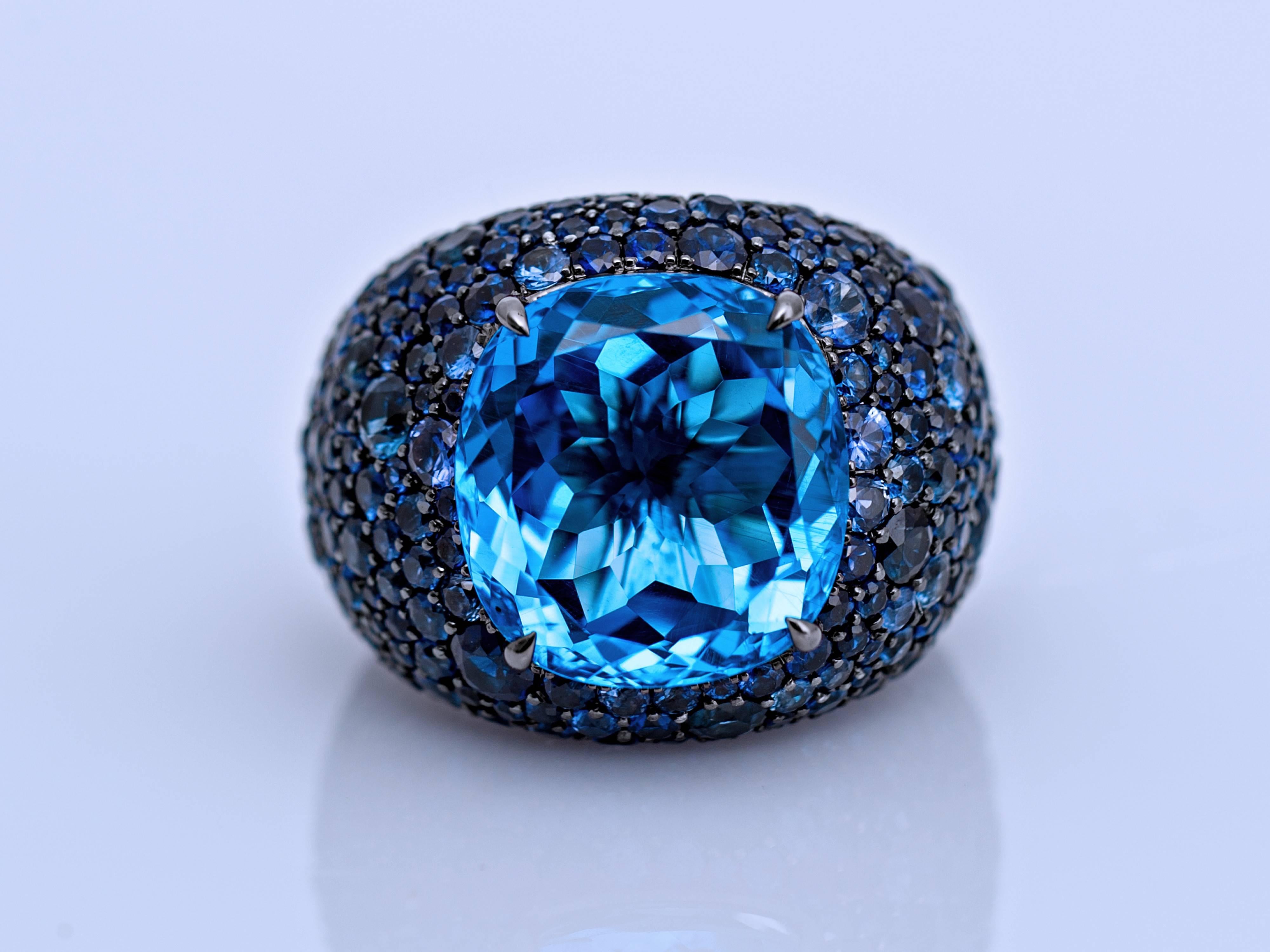 Focusing on the centre of the 18k white gold ring, a cushion shaped 14.24 Carat London Blue Topaz surrounded by 311 round sapphires in different sizes. Capturing its beauty through the mixtures of dark and light blue.