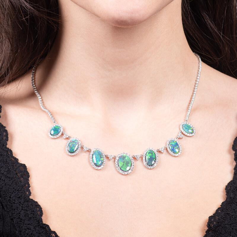 This exquisite opal necklace features 14.27ct total weight in oval cut, natural black opals from Lightning Ridge, Australia, accented by 6.37ctw in round brilliant cut, natural diamonds that form halos around the opals and line the necklace. The