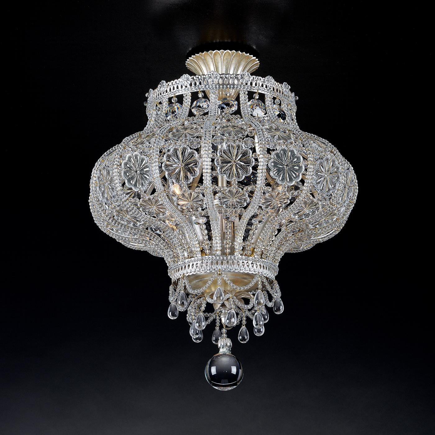S'inspirant des lanternes du Moyen-Orient, ce plafonnier affleurant est entièrement fabriqué en Italie. Avec des cristaux de verre aux formes variées, le pendentif est complété par un revêtement de feuilles d'argent pour un maximum de brillance.