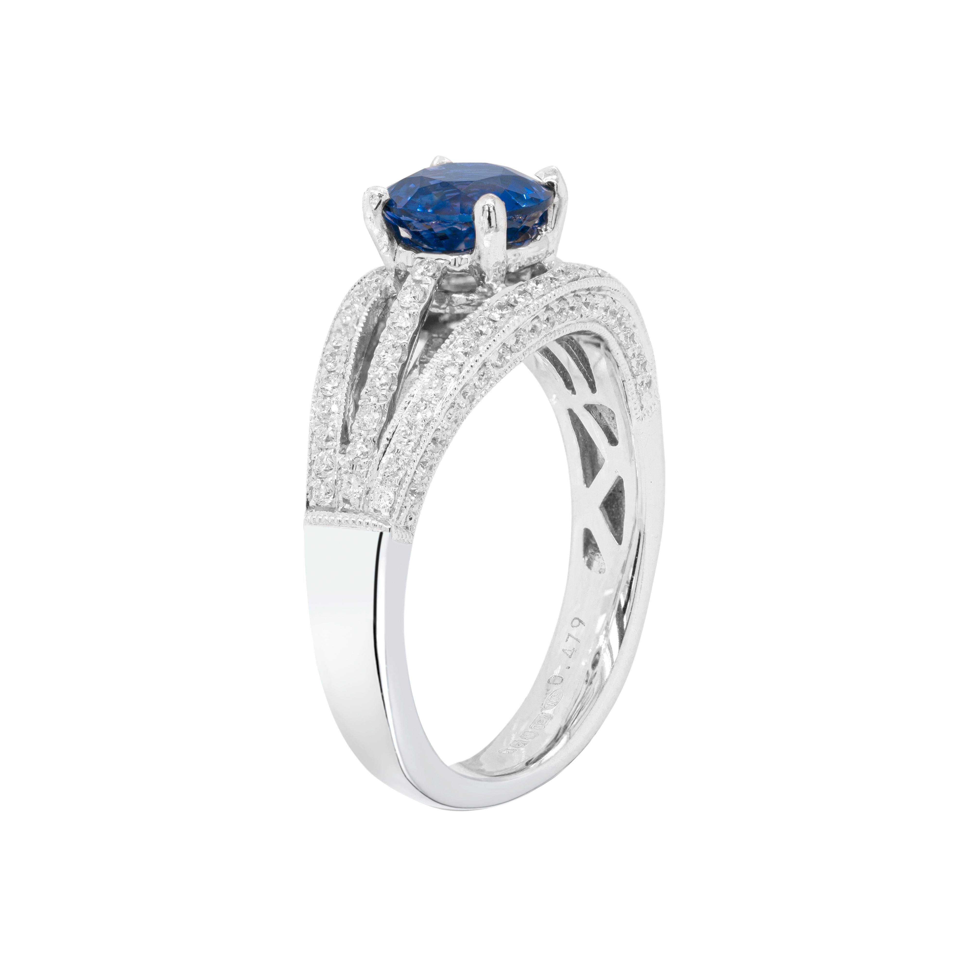 This stunning engagement ring features a vibrant round royal blue sapphire in the centre weighing 1.42ct mounted in a four claw, open back setting. The gorgeous stone is set within a three row diamond set 18 carat white gold mount tapering to a fine