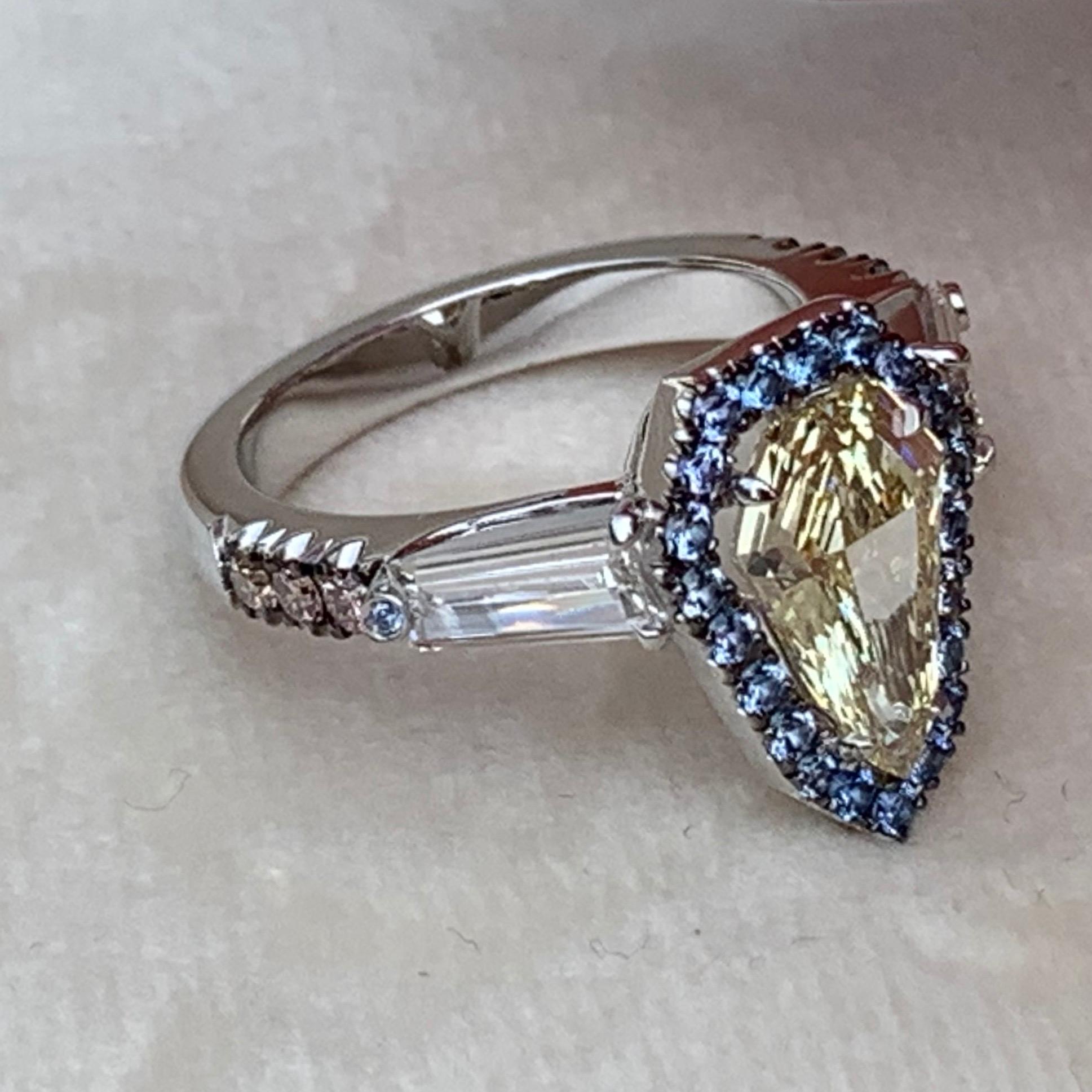 One of a kind handmade ring in 18K White gold 7,5 g. Set with a GIA certified Fancy Light Yellow Shield-Cut Diamond centerstone 1,43 carat., VVS2, Entourage pave set with Unheated Burma Blue Sapphires 0,345 ct. ( These Sapphires stay bright in the
