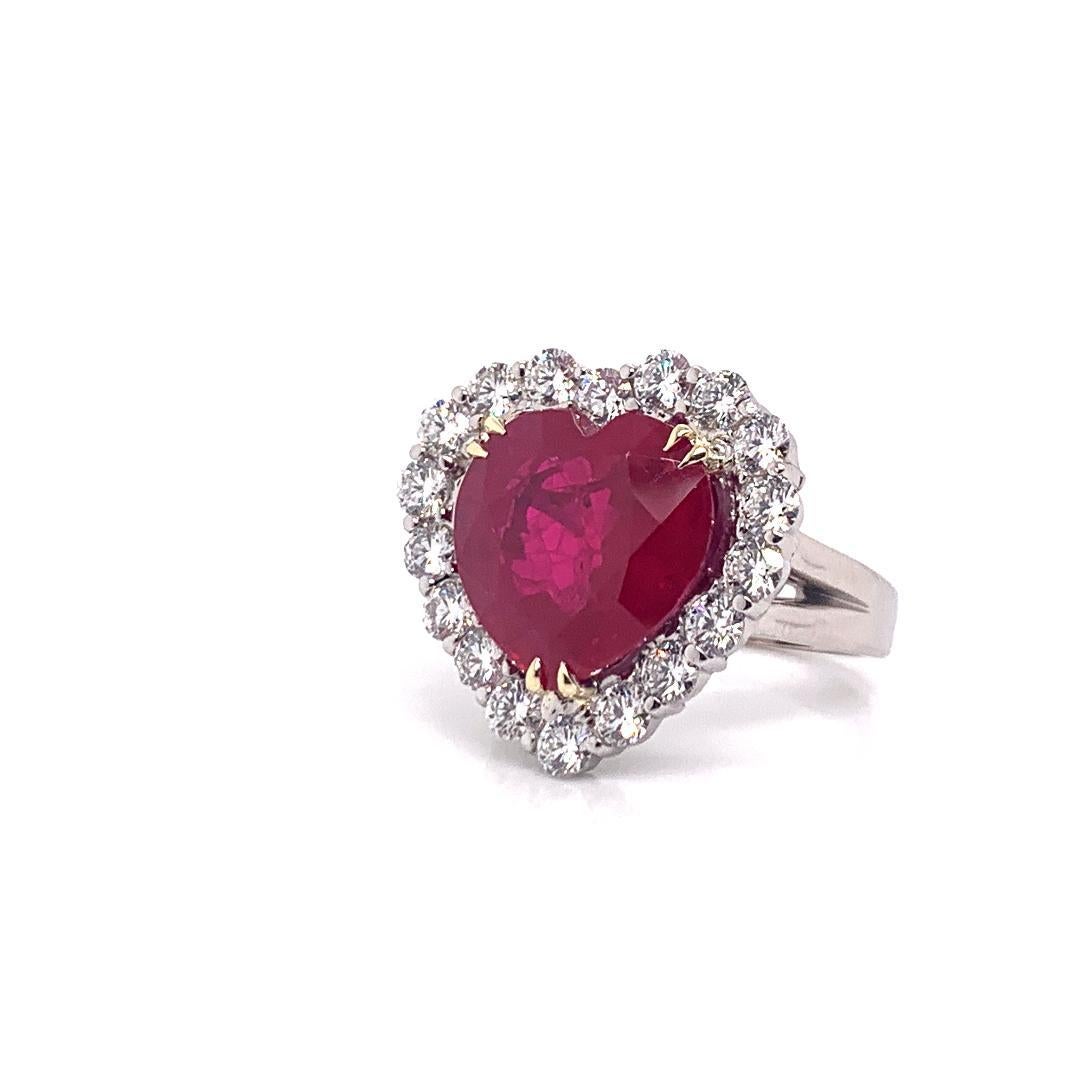 Magnificent, very large, 11.75 carat heart shaped vivid red faceted corundum ruby estate cocktail ring is talon prong set in 18 karat yellow gold and surrounded by prong-set super sparkly round brilliant white diamonds set in 18 karat white gold.