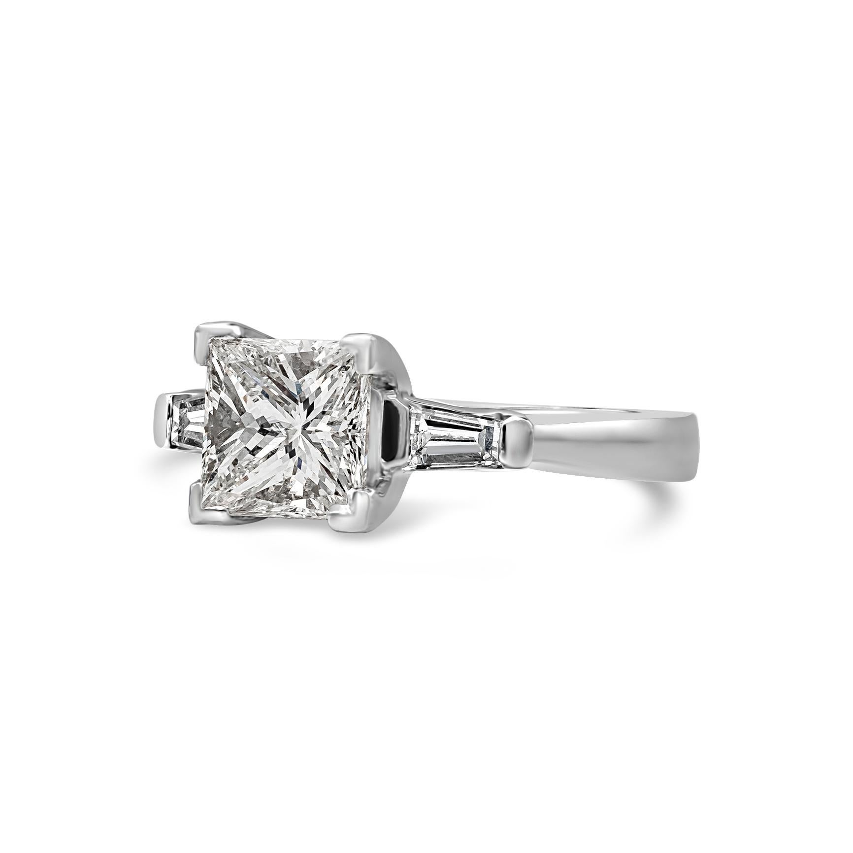 Un style de bague de fiançailles intemporel et populaire, mettant en valeur un diamant de taille princesse de 1,44 carat, flanqué d'un diamant baguette classique effilé d'un poids total de 0,26 carat, serti de part et d'autre de la bague. EGL USA a