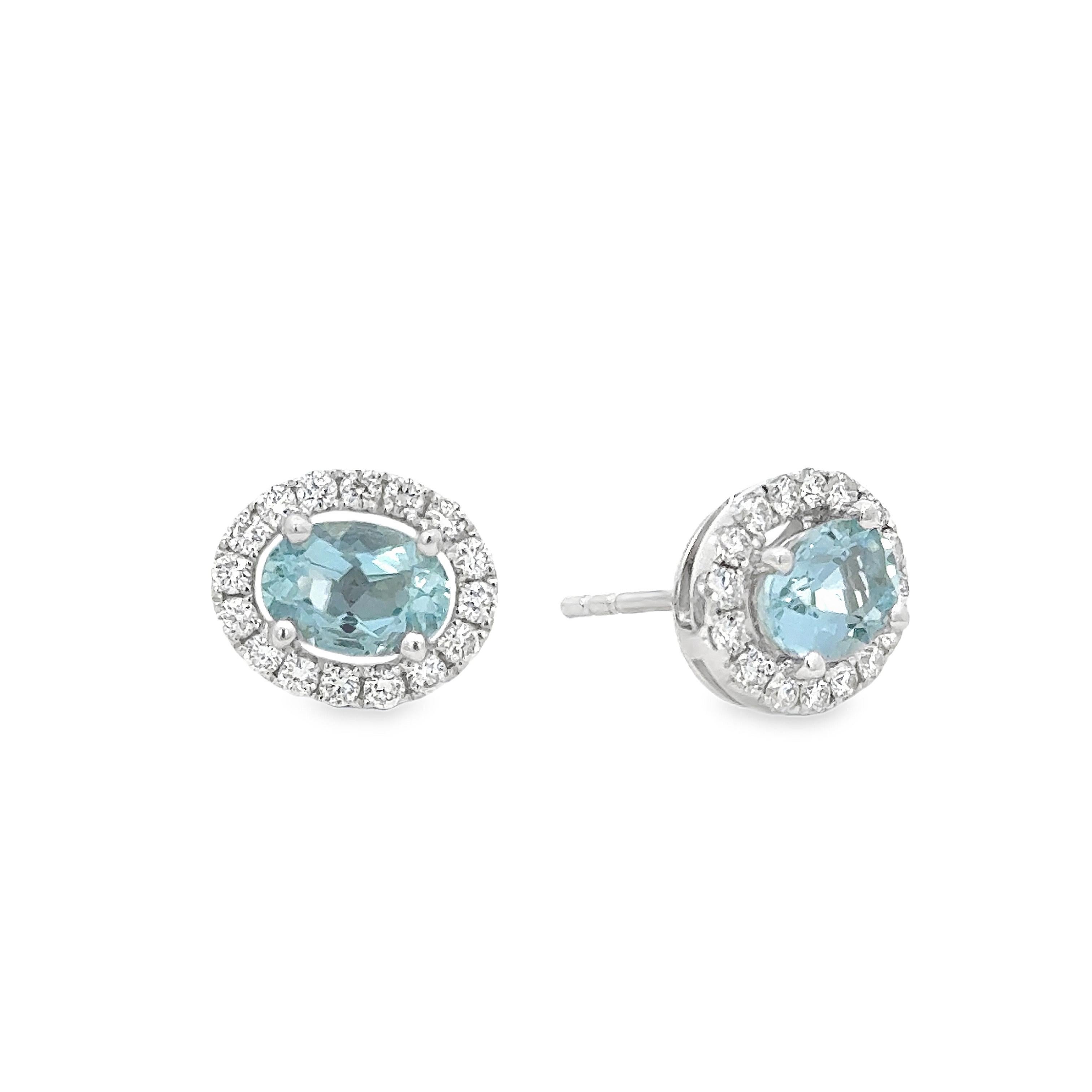 A fashionable pair of stud earrings, featuring oval cut aquamarines weighing 1.44 carats total, each set on four rounded prongs. Accented by halos of round cut diamonds weighing 0.46 carat total, set on an open-work design. Finely made with 18K