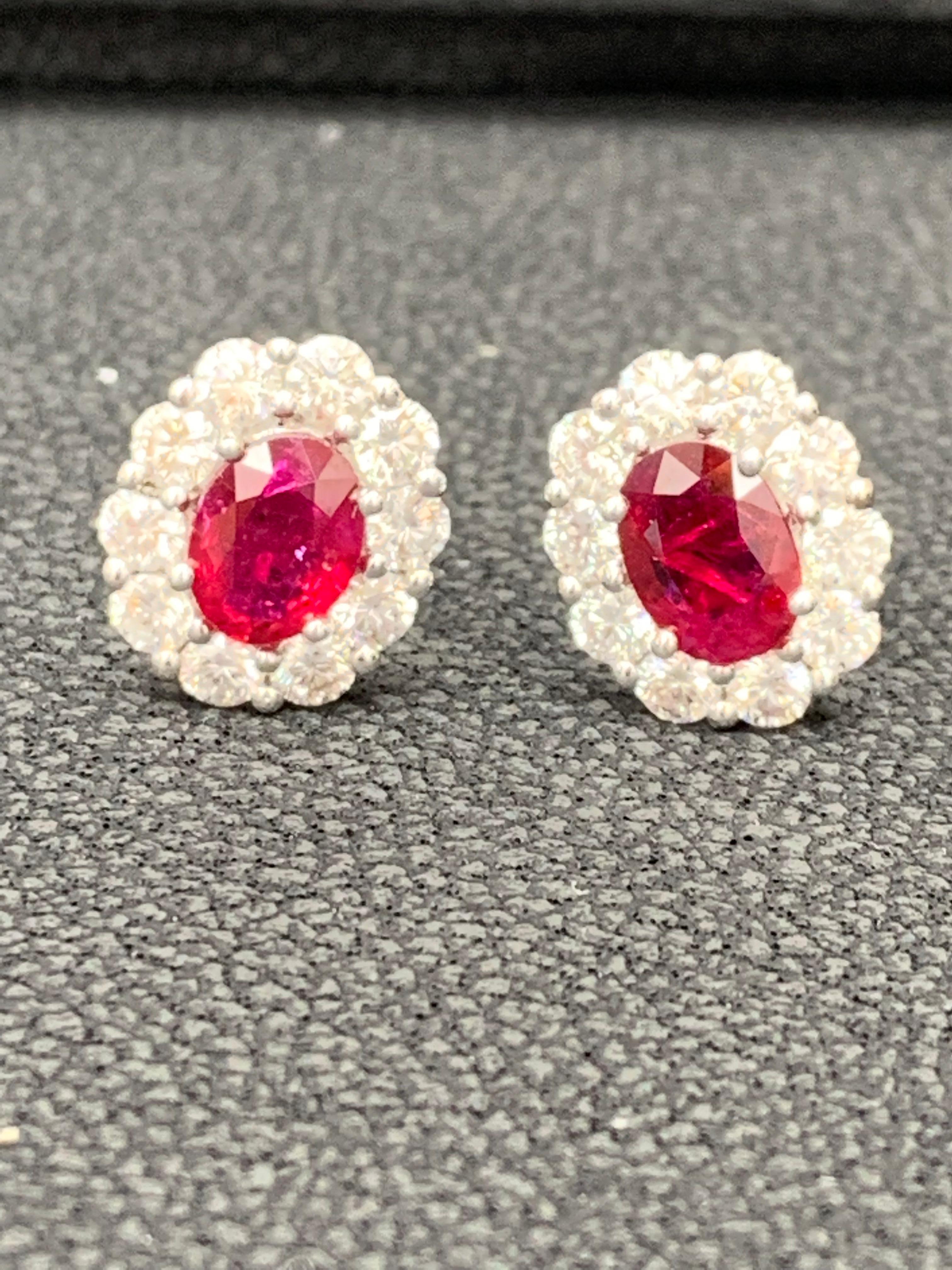 A simple pair of stud earrings showcasing 1.45 carats of oval cut red rubies, surrounded by a single row of 20 round brilliant diamonds weighing 1.35 carat. Made in 18 karat white gold.