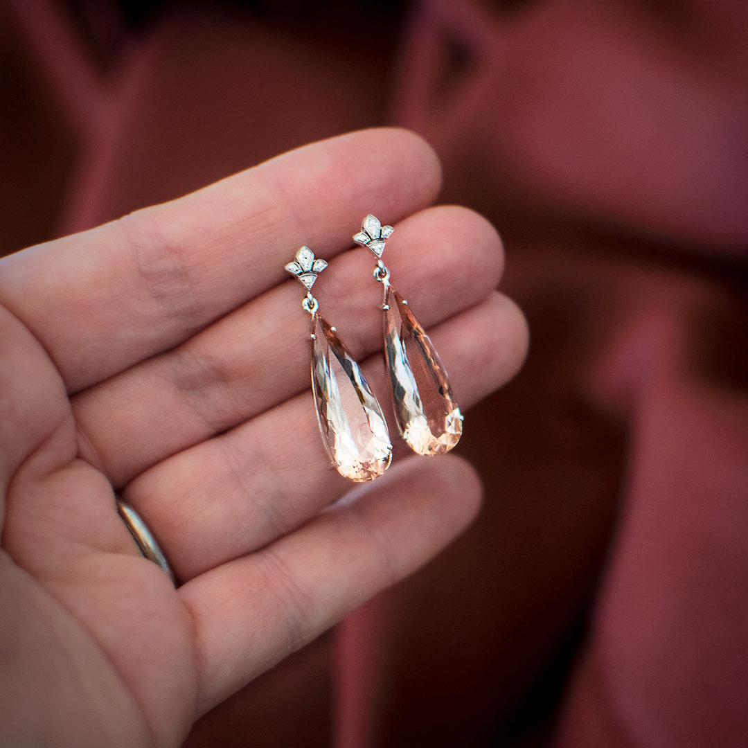 A stunning pair of pear shaped Morganites fascinates with their soft peachy pink colour. They are beautifully offset by Fleur De Lis diamond fittings. The Morganites weigh a total of 14.56 carats and the total diamond weight is 0.28 carat, Colour