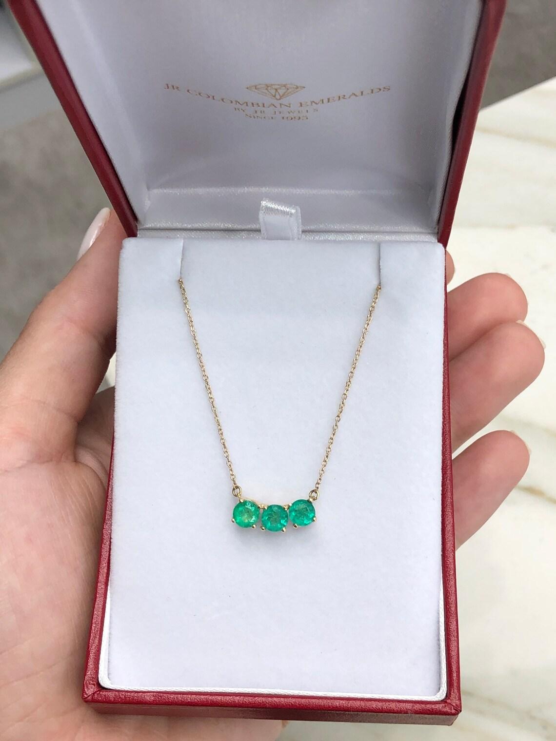Una straordinaria collana a tre pietre di smeraldo colombiano in oro giallo 14K. 1,45tcw di puro verde vibrante sono mostrati in questa gemma estratta dalla terra. Un semplice e pulito cestino a quattro punte contiene ogni gemma. La nostra