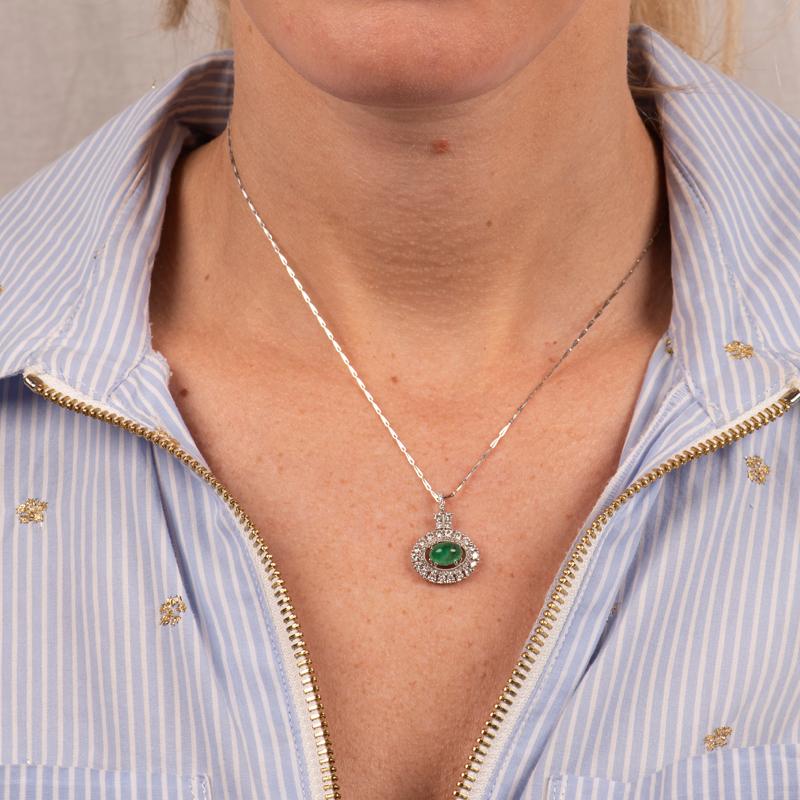 This 18 karat white gold pendant features a 1.47 carat oval cabachon emerald surrounded by a double halo in 0.90 carat total weight in round brilliant accent diamonds finished with milgrain detailing. It is set on a 16