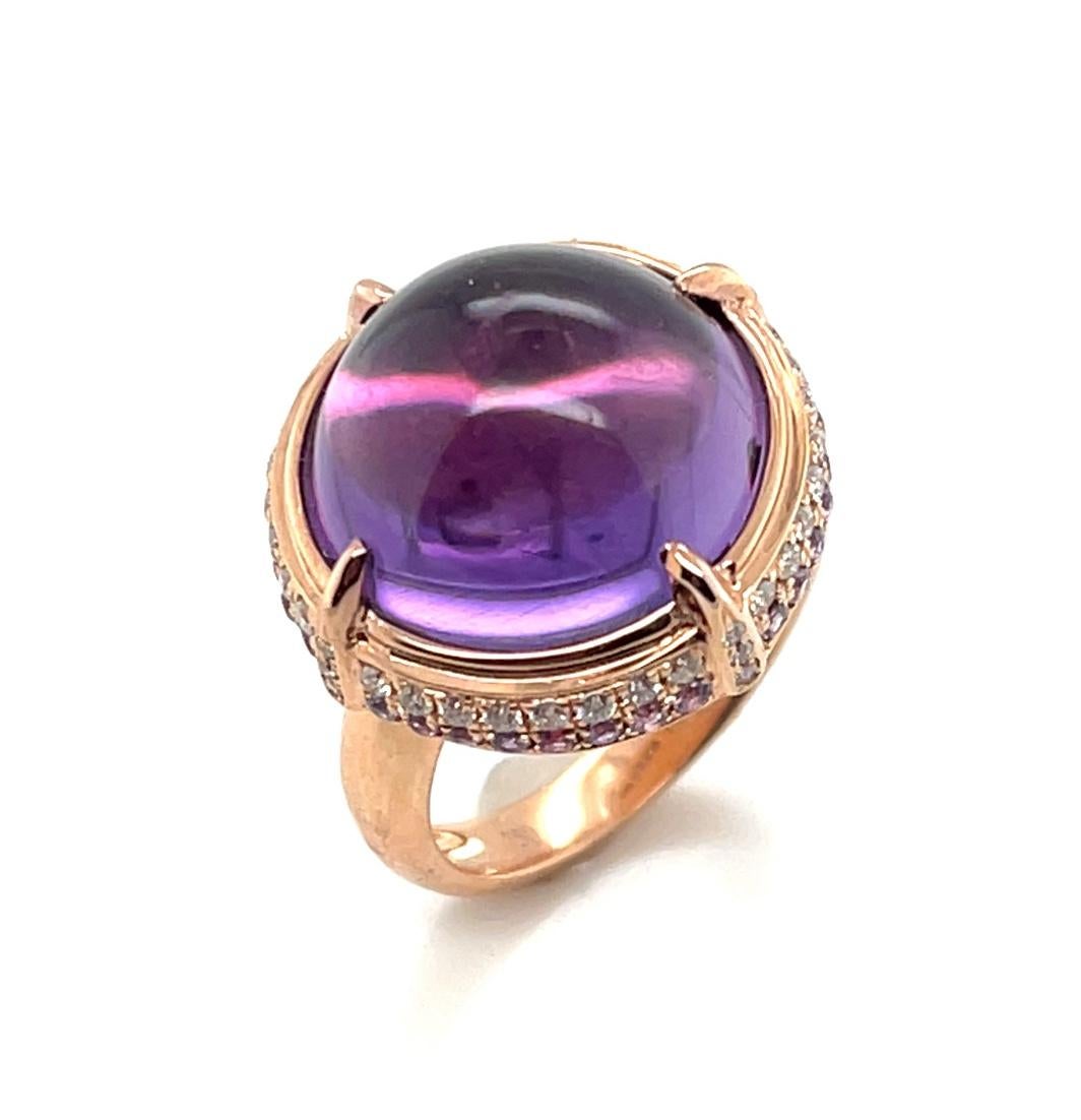 This striking ring features a 14.70 carat amethyst cabochon set in rose gold with bright pink sapphires and diamonds. The amethyst has beautiful crystalline purple color with pinkish highlights, accentuated by the 18k rose gold setting. A row of