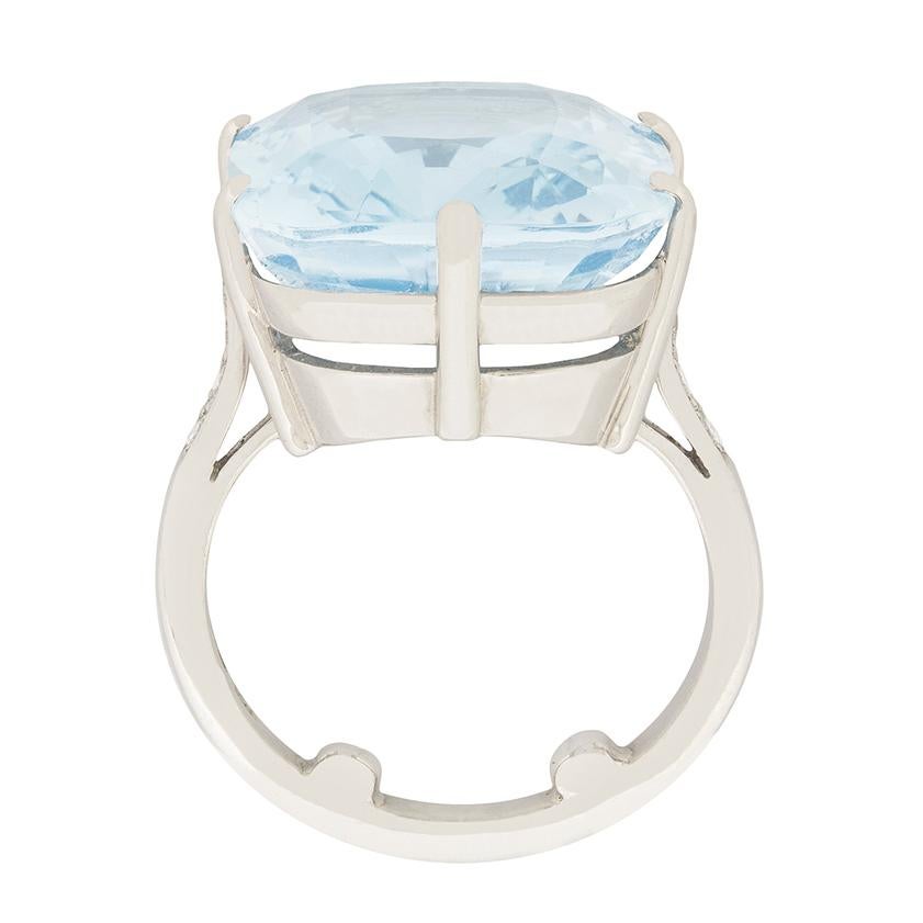 A sky blue cushion cut aquamarine, weighing 14.71 carats, glistens boldly between diamond set shoulders at the centre of this dramatic statement ring dating from the 1980s.

The ring’s setting is comprised of 18 carat white gold with a petite
